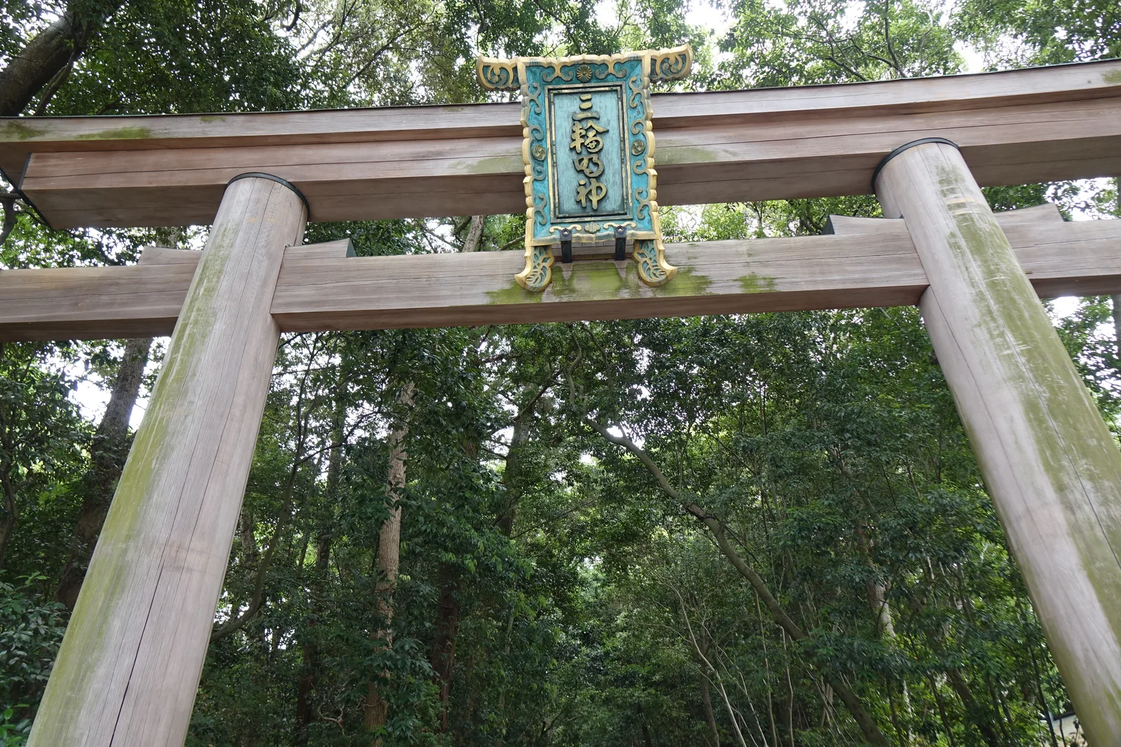 大神神社二之鳥居的扁額特寫，青綠底金框，直書「三輪明神」，鳥居柱身長著綠苔