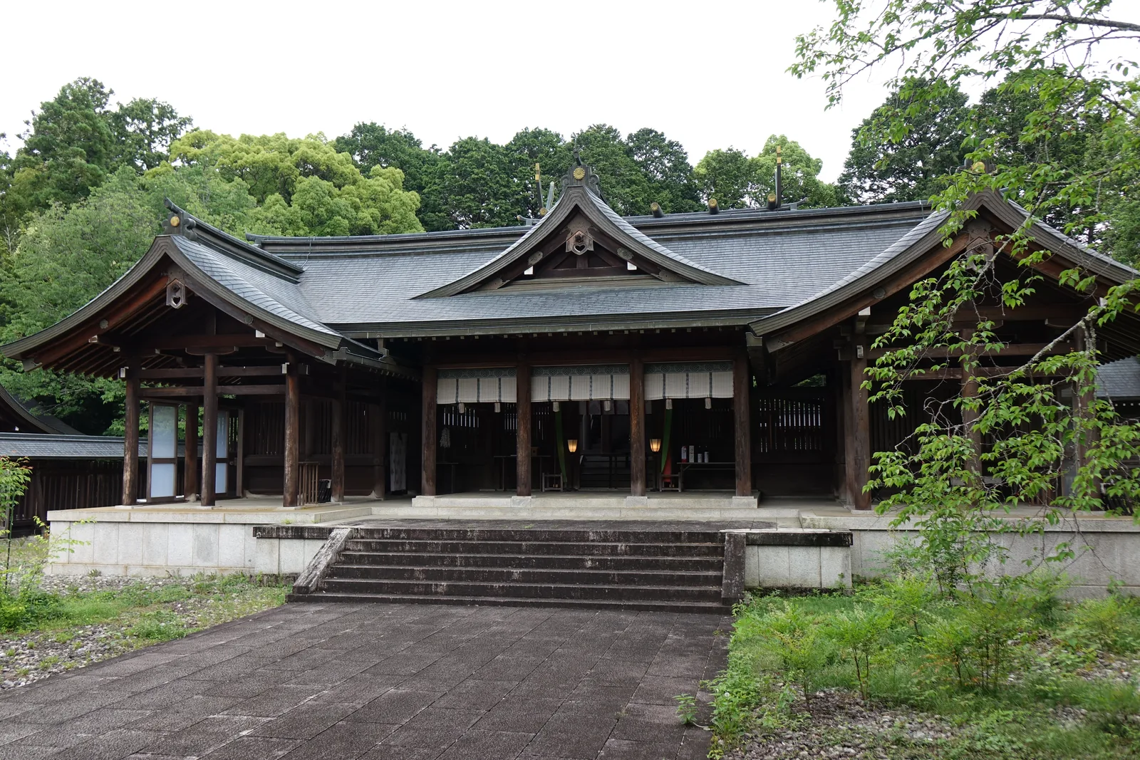 吉野神宮的拜殿正面，橫長的入母屋造建築，中央起千鳥破風，屋頂是鏽成青綠的銅板，兩側各接一段廻廊