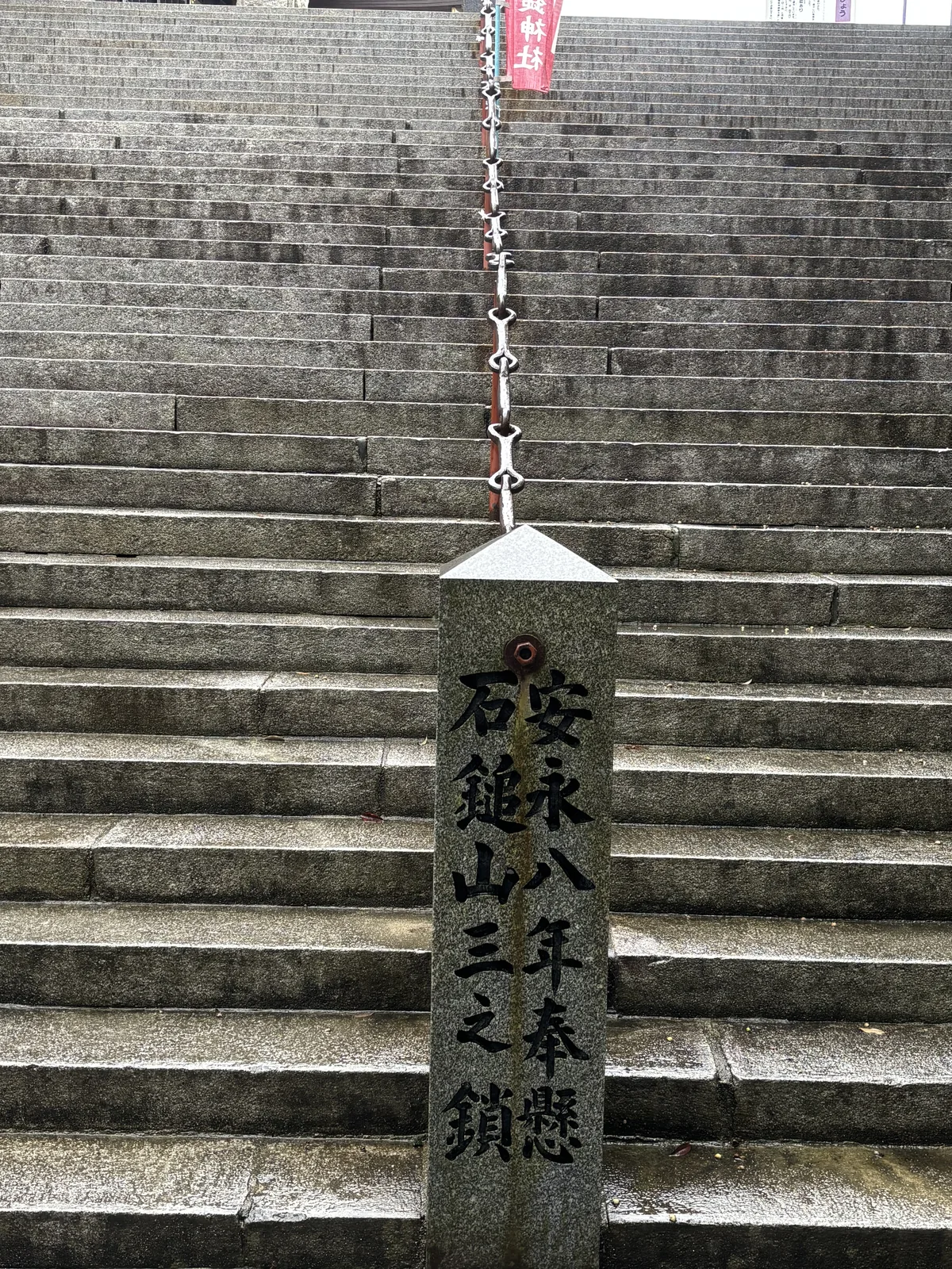 石鎚神社本社的花崗岩石段，中央從上到下垂著一條鐵鏈，下端固定在一根尖頂石柱上，柱面刻著「安永八年奉懸　石鎚山三之鎖」