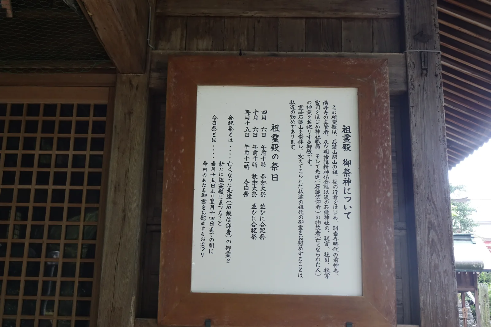 祖靈殿門柱上的白底黑字木框掲示，寫著御祭神與祭日：四月六日、十月六日的春秋季大祭並合祀祭，每月十五日上午十一時的命日祭