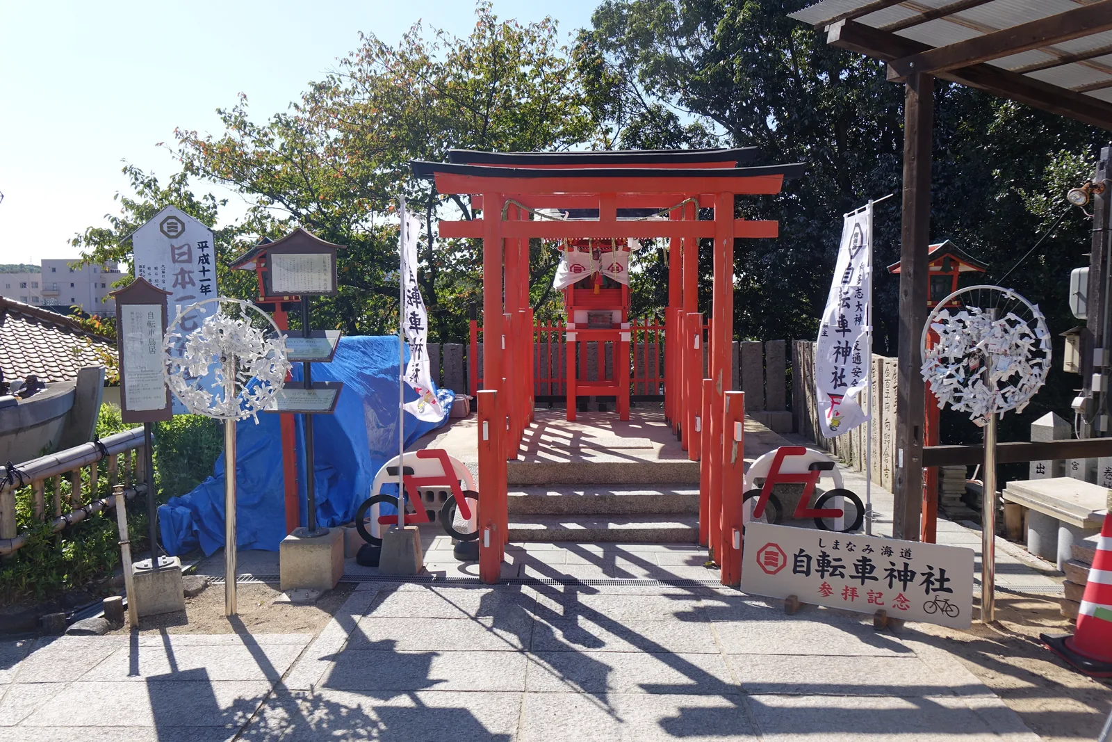 因島大山神社的和多志神社，三座紅鳥居並排在一段短石段上，盡頭是紅色的小社殿，前方立著「しまなみ海道　自転車神社　参拝記念」的木牌，兩側各擺一台紅白的自行車