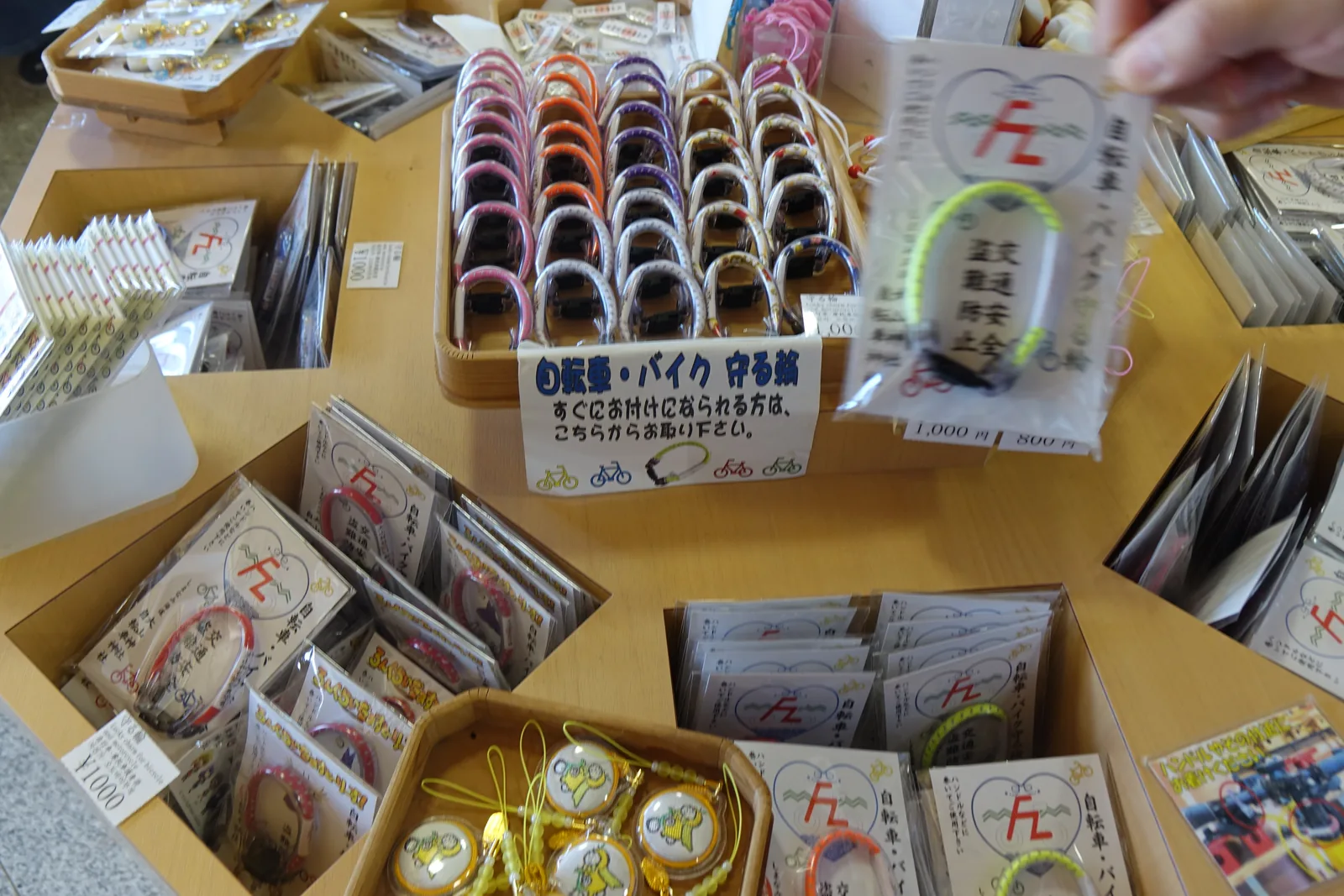 大山神社授与所桌上的「自転車・バイク　守る輪」，一整盤彩色的環，周圍是自行車御守與社紋貼紙型御守