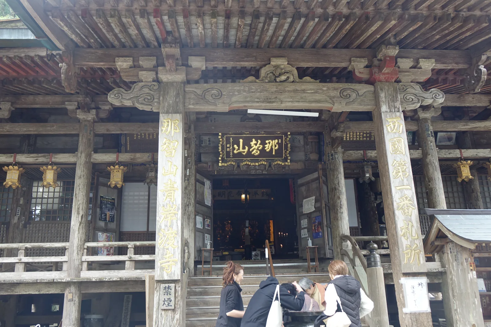 那智山青岸渡寺本堂正面，一寸漆也不上的素木造，木肌被雨與香煙燻成灰褐色，扁額寫「那智山」，右柱刻「西國第一番札所」