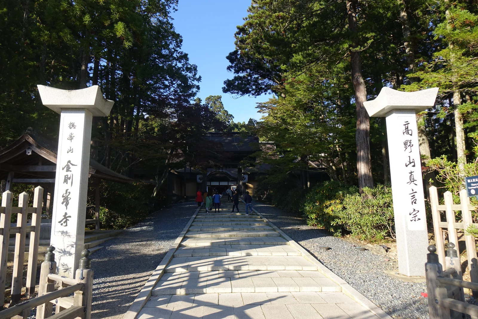 金剛峯寺參道口的一對石標，右刻「高野山真言宗」左刻「金剛峯寺」，石板路緩緩上升，盡頭是正門