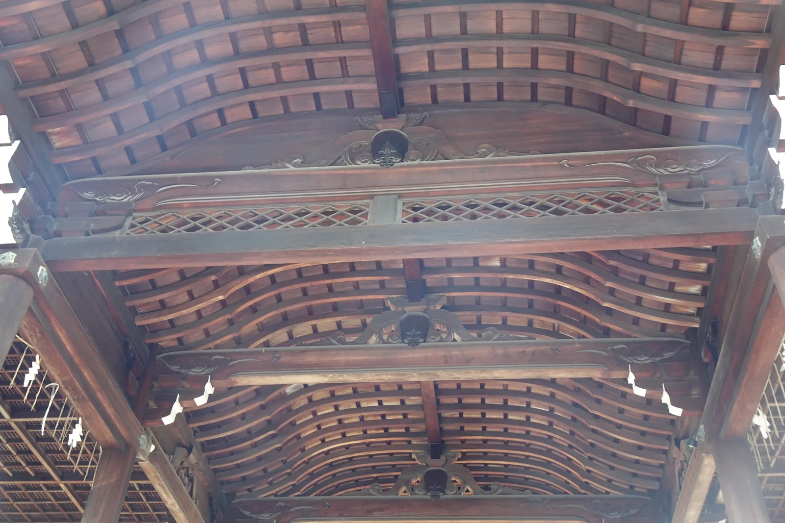 近江神宮樓門的天井仰視：三層彎曲的垂木一層層退進去，之間夾著蟇股雕刻與格狀組物，兩側垂著紙垂