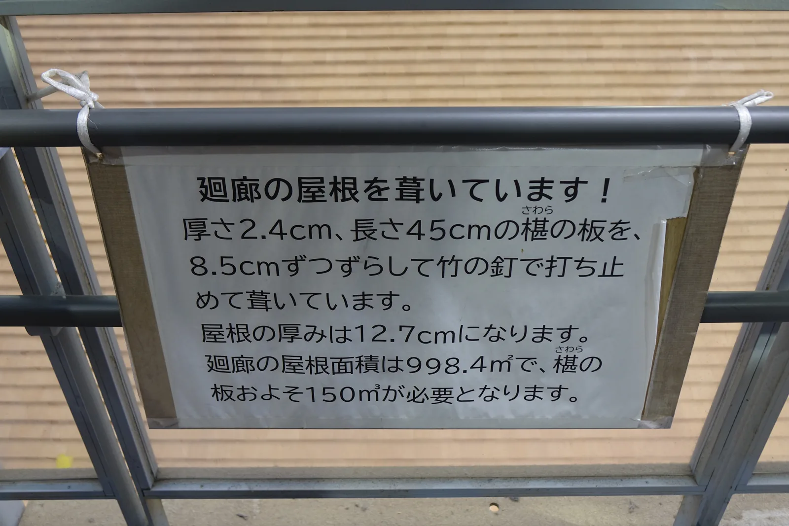 掛在修學台欄杆上的護貝說明：「廻廊の屋根を葺いています！」，寫著厚 2.4 公分、長 45 公分的椹板每次錯開 8.5 公分、用竹釘打止，屋頂厚 12.7 公分、面積 998.4 平方公尺