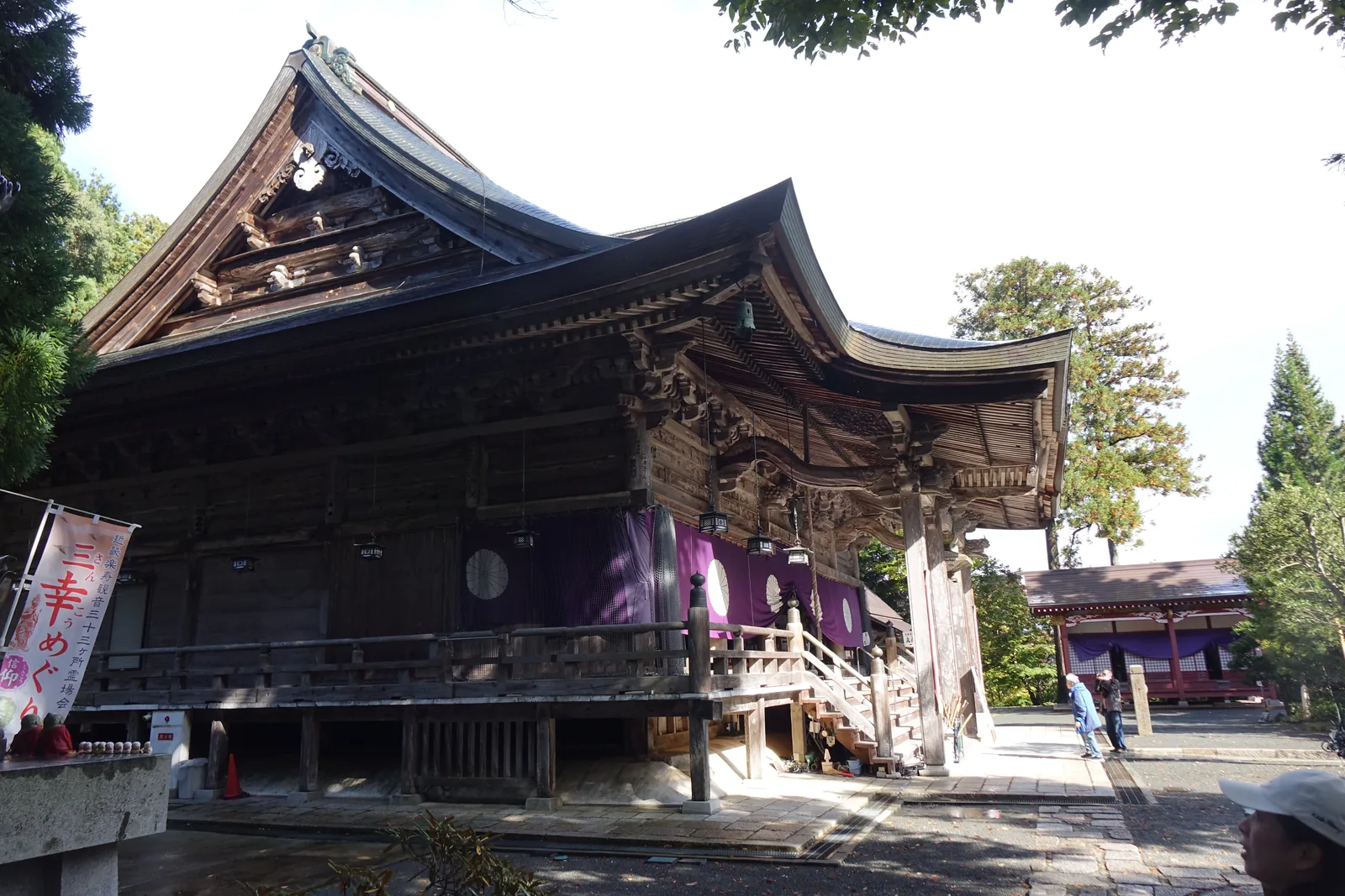 成相寺本堂側面：整棟坐在從坡面挖出來的平臺上，前面沒有廣場，左側掛著「三幸めぐり」的幟旗