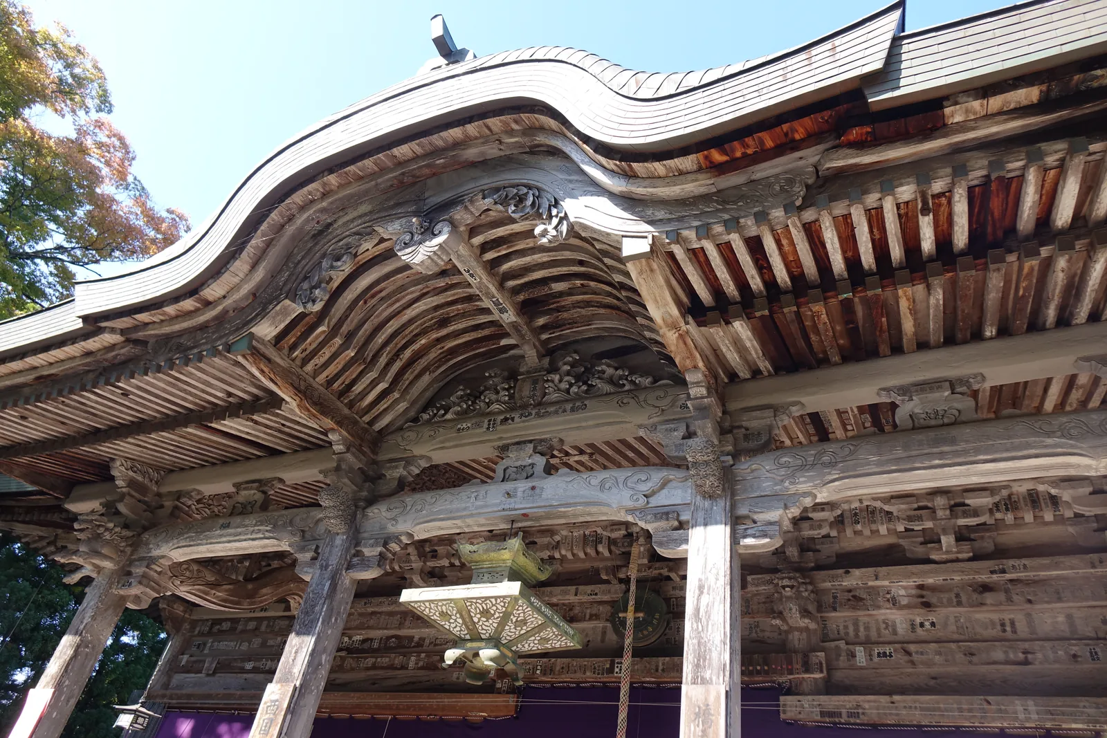 成相寺本堂唐破風下的斗栱與木鼻，層層向外挑出，虹梁上滿是浮雕，梁面密密貼著奉納札