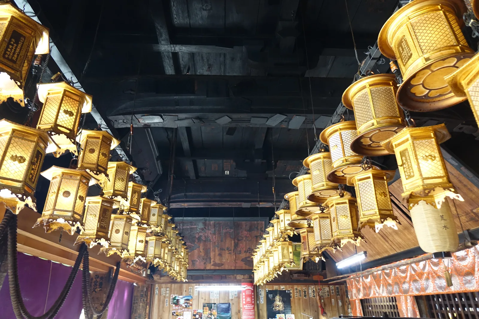 成相寺本堂外陣：黑透了的梁下吊著兩列金色燈籠，一排排往深處排過去，紫幕上是白色的菊紋