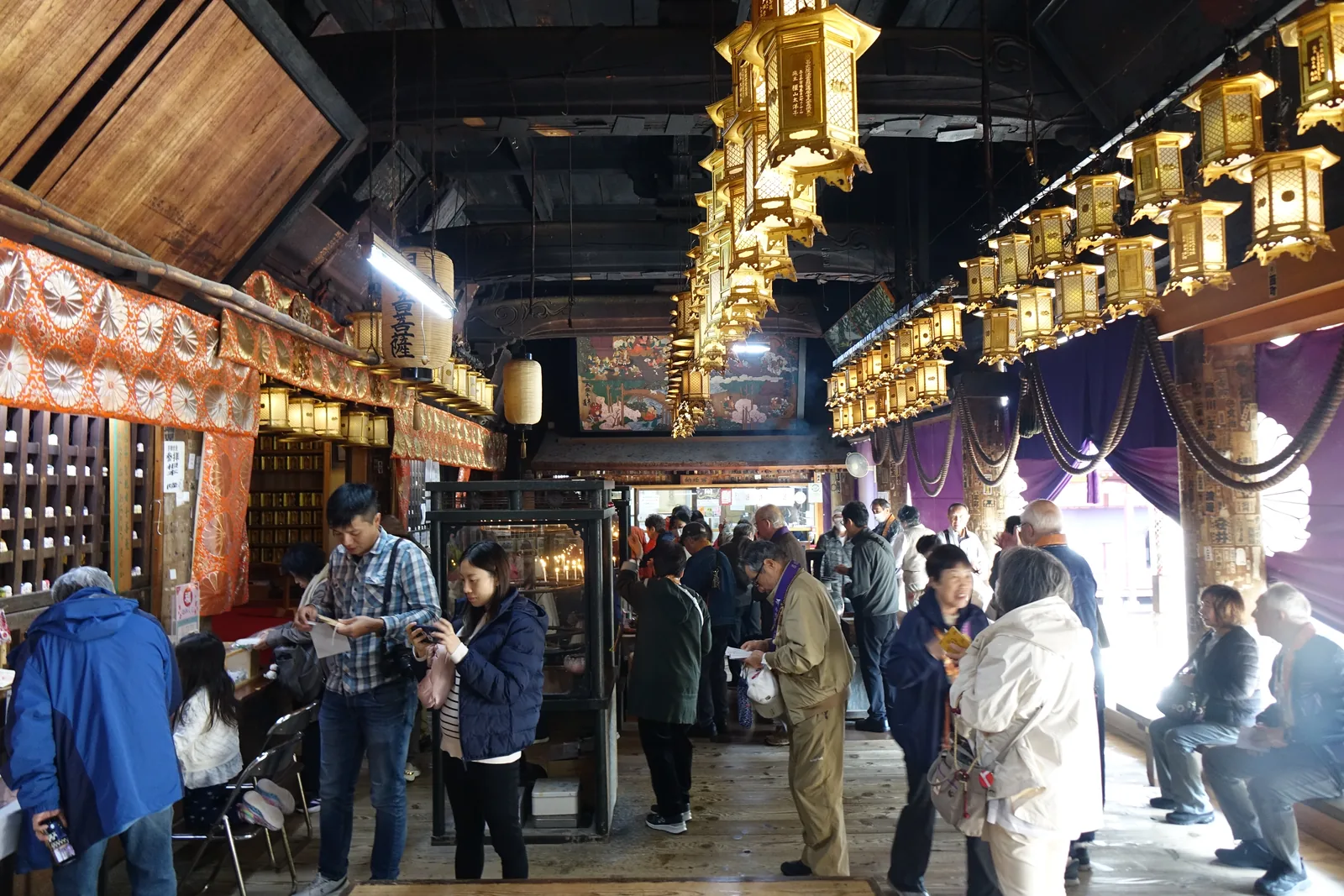 成相寺本堂外陣深處的納經所，參拜者排隊受朱印，柱子上貼滿千社札，玻璃櫃裡點著蠟燭