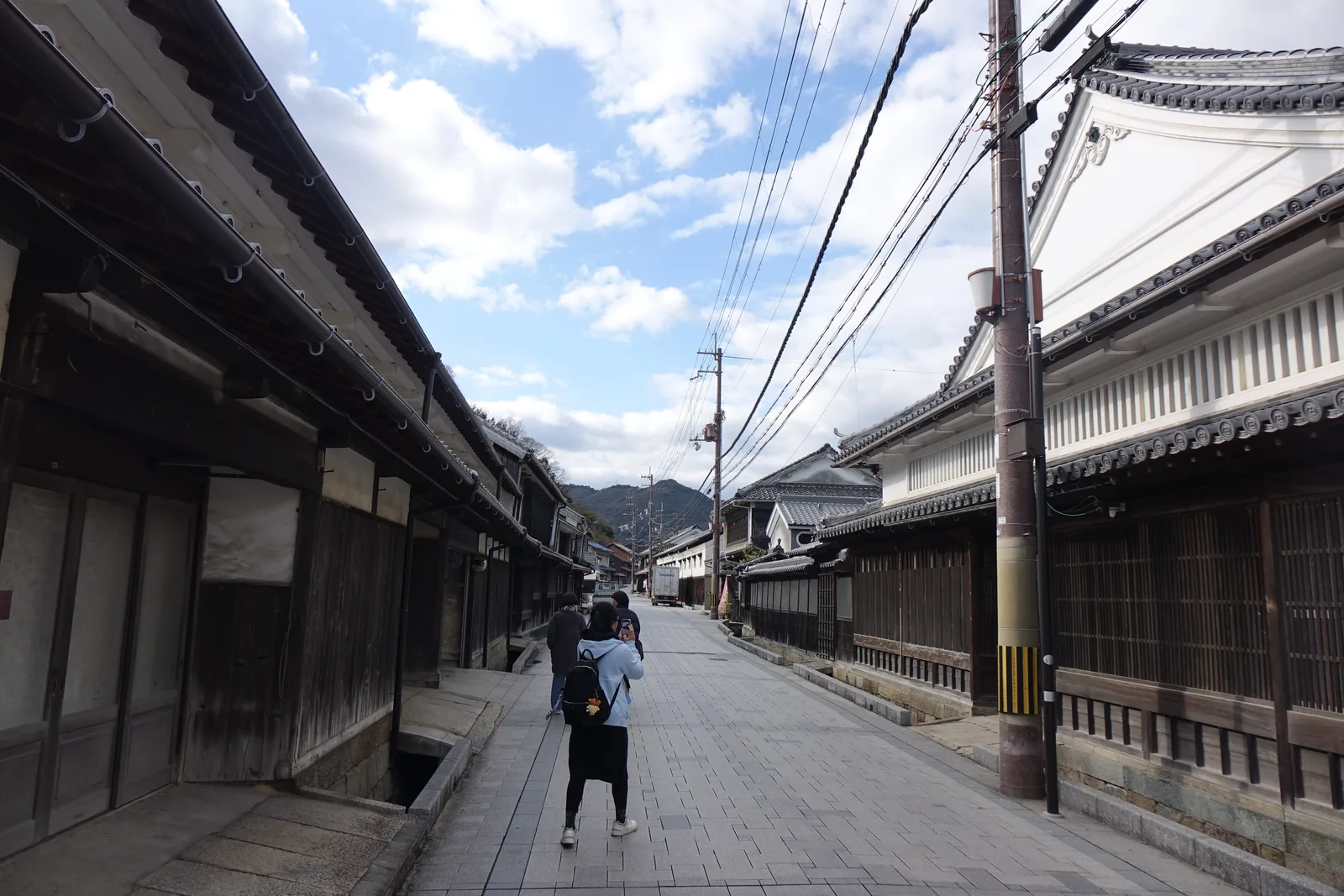 坂越的主街「大道」：町家與白牆的土藏夾著一條往海下坡的路，盡頭是山，路上有兩名行人
