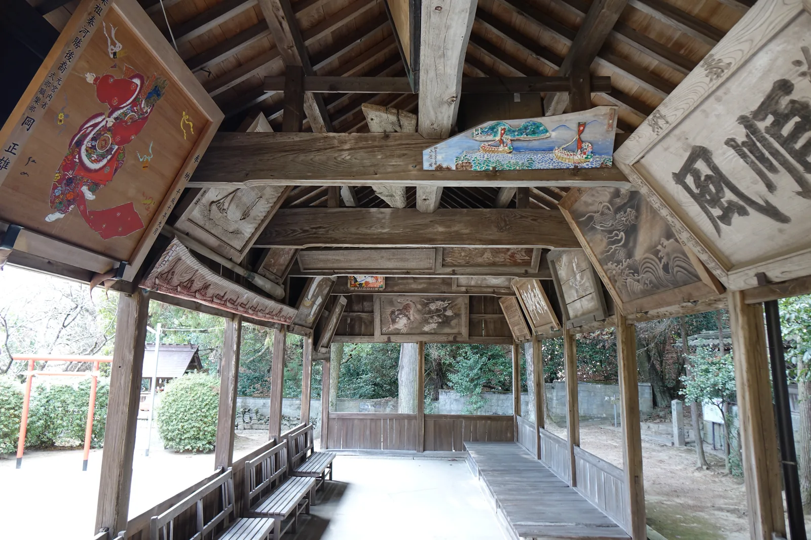 大避神社拜殿兩翼的繪馬堂：四面不封的長廊，柱間全是空的，屋頂下架著疏朗的小屋組，梁上掛著繪馬與扁額