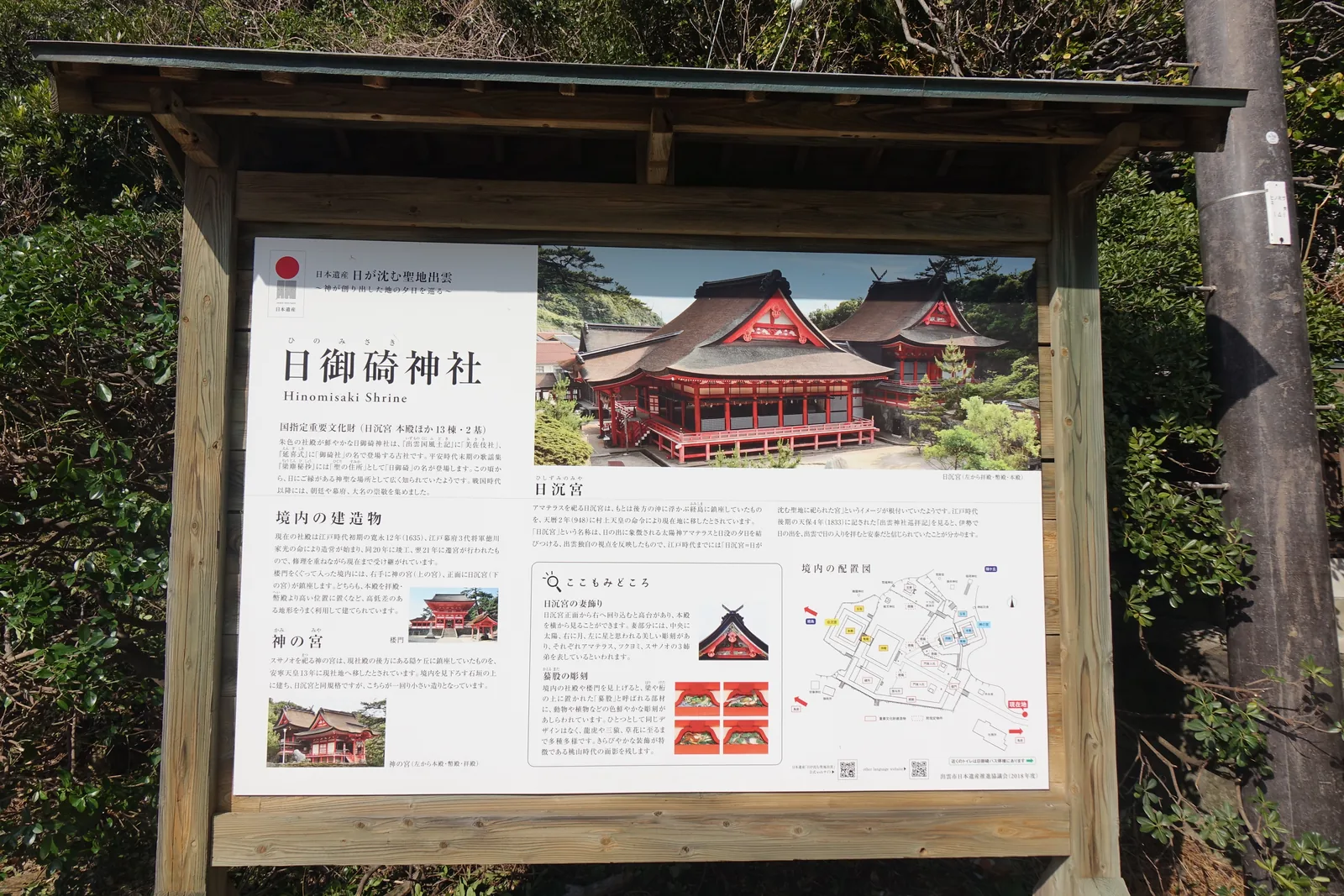 出雲市日本遺產推進協議會設置的解說板，屬「日が沈む聖地出雲」（日落的聖地出雲）這條故事線。板上標明國指定重要文化財的範圍是「日沈宮 本殿ほか13棟・2基」（日沈宮本殿以外另十三棟、二基），並把日沉宮從經島遷來（天曆2年／948）、神の宮從隠ヶ丘遷來（安寧天皇13年）兩件事分欄寫清楚。右下角是境內配置圖。