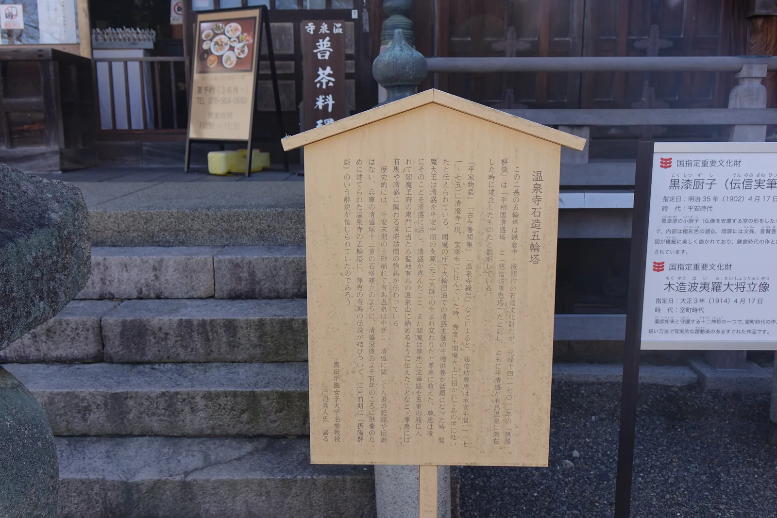 本堂前並排的三份說明。中央的木牌由園田學園女子大學名譽教授田邊眞人所書，指出《攝陽群談》把兩基塔說成平清盛所建，但歷史上清盛既無入湯紀錄也無傳說。右側是國指定重要文化財的案內板，列著黑漆厨子與木造波夷羅大將立像。左後方的幟寫「温泉寺　普茶料理」，A 字看板寫要預約三名以上、營業時間十一點半到一點半。