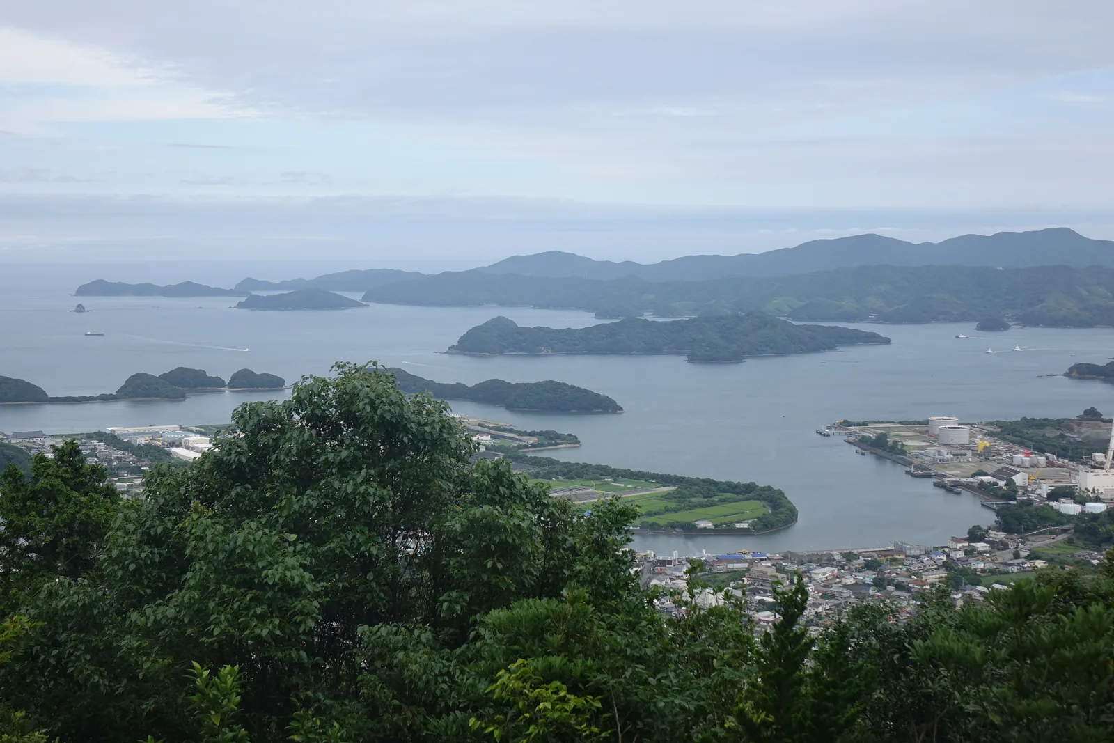 從津峯山山頂的展望台往東看橘灣：海面被幾道低矮的半島與沙洲切開，聚落沿著水邊排成細長的一條，遠處是紀伊水道