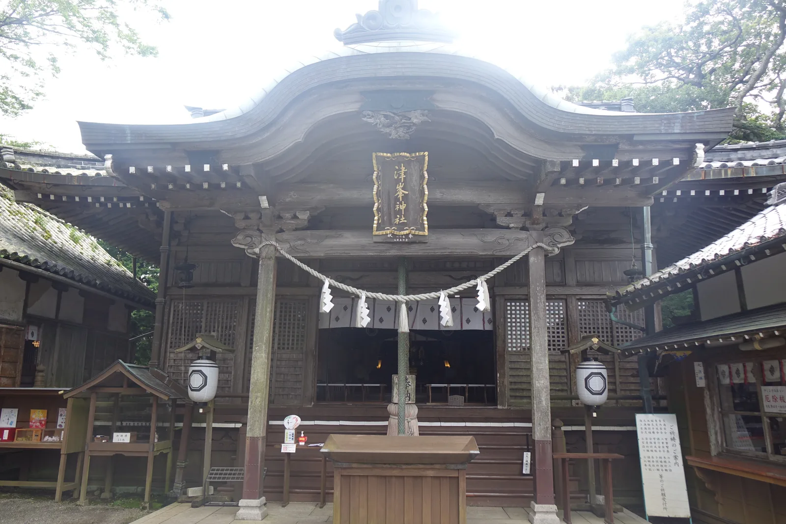 津峯神社拜殿正面：唐破風的屋頂、扁額寫著「津峯神社」、兩盞掛燈籠，兩側是授与所與掲示板