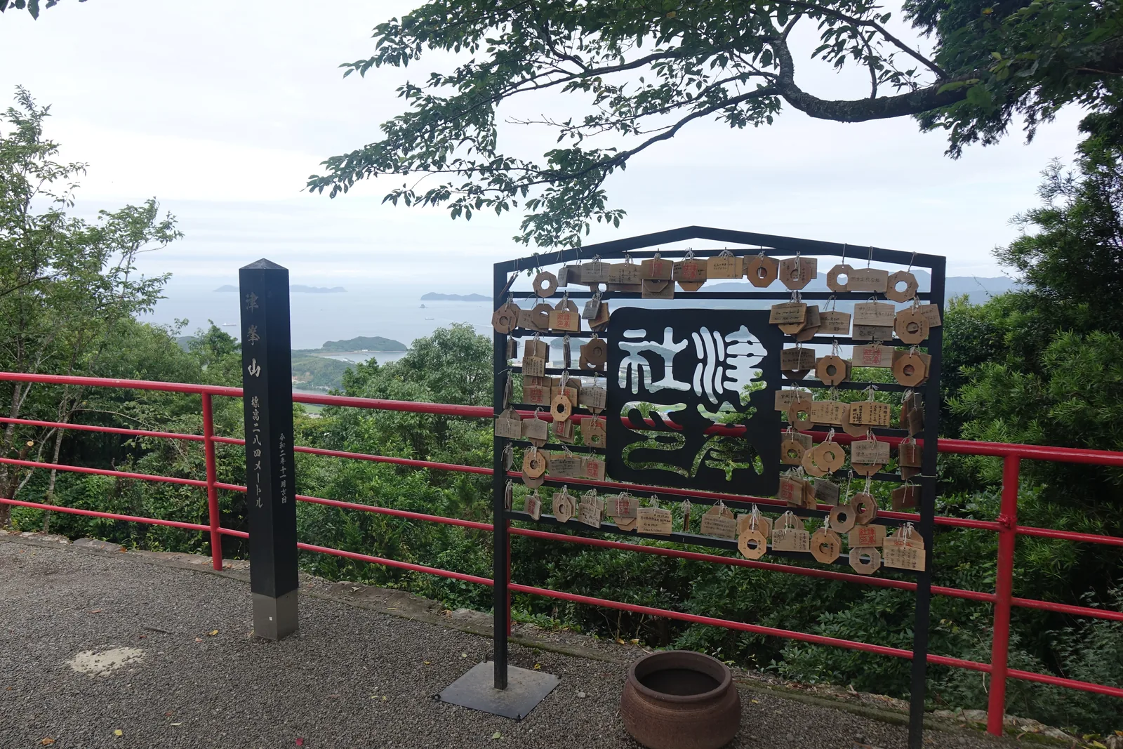 津峯山山頂的標柱與繪馬掛：標柱刻著「津峯山　標高二八四メートル　令和二年十一月吉日」，旁邊的鐵架掛滿中央開孔的六角形繪馬，鐵板本身鏤空成篆體的社名