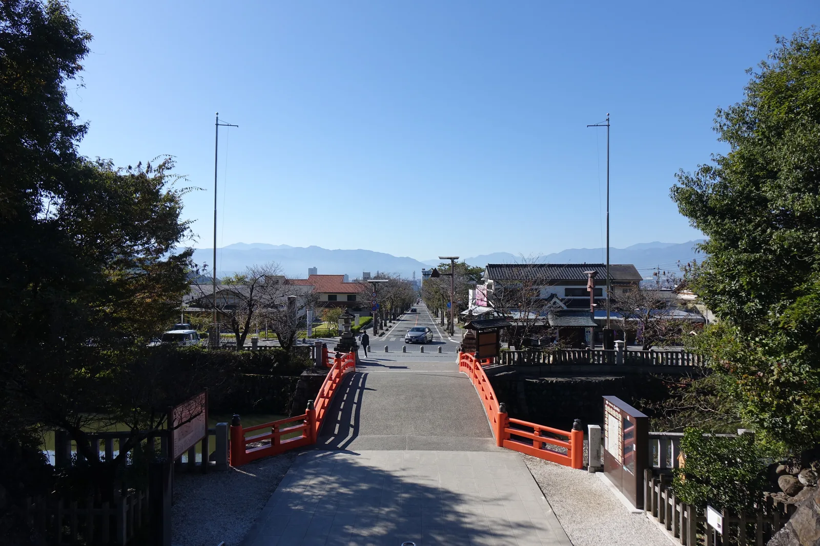 從參道口往南看。武田通り筆直往下延伸兩公里多，兩側是住宅與行道樹，盡頭是甲府市街與盆地，更遠處是南邊的山稜。神社標高三五三公尺，甲府驛二七五公尺——這條路的方位是十九度，兩千一百五十九公尺沒有一個彎。