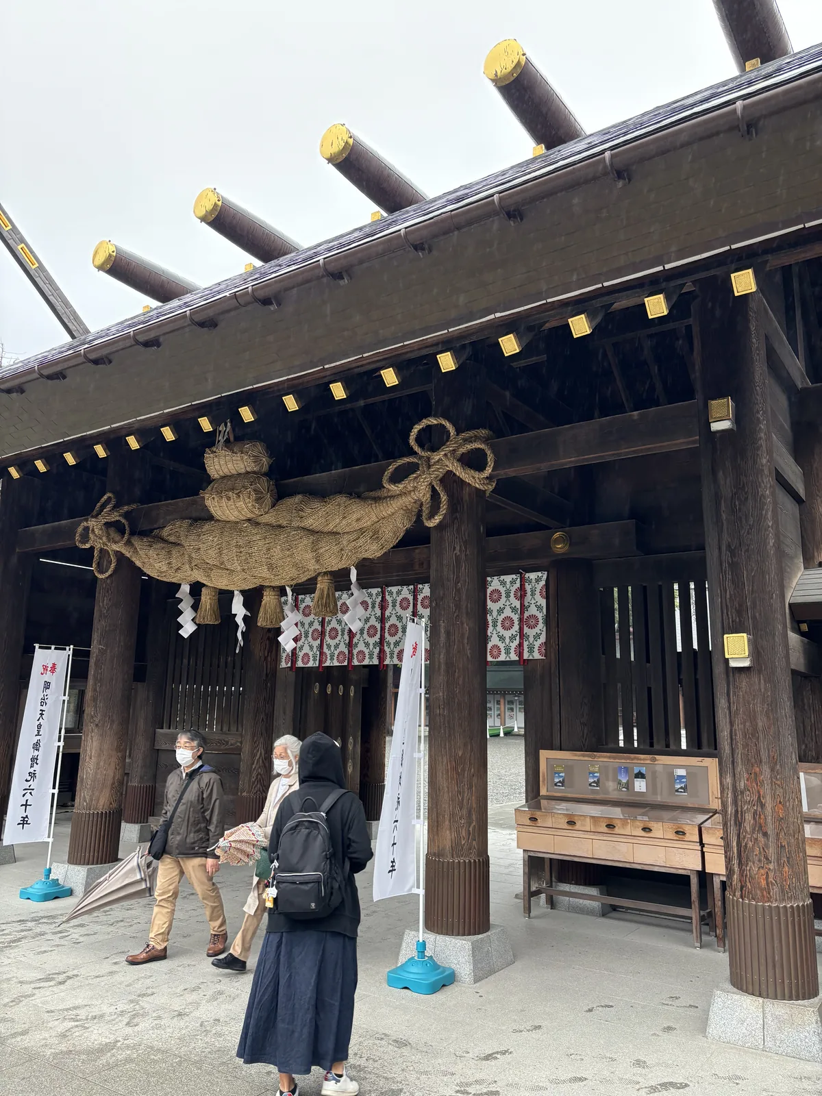 北海道神宮神門下的大注連繩與白幟，幟上紅字「奉祝」、墨字「明治天皇」