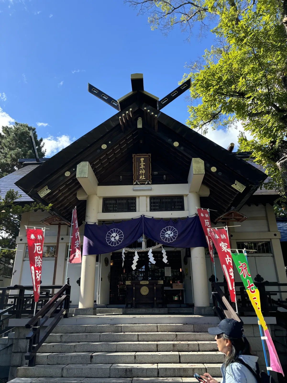 豐平神社拜殿，屋脊兩端立著交叉的千木，向拜下垂著紫幕，兩側插滿奉納的幟
