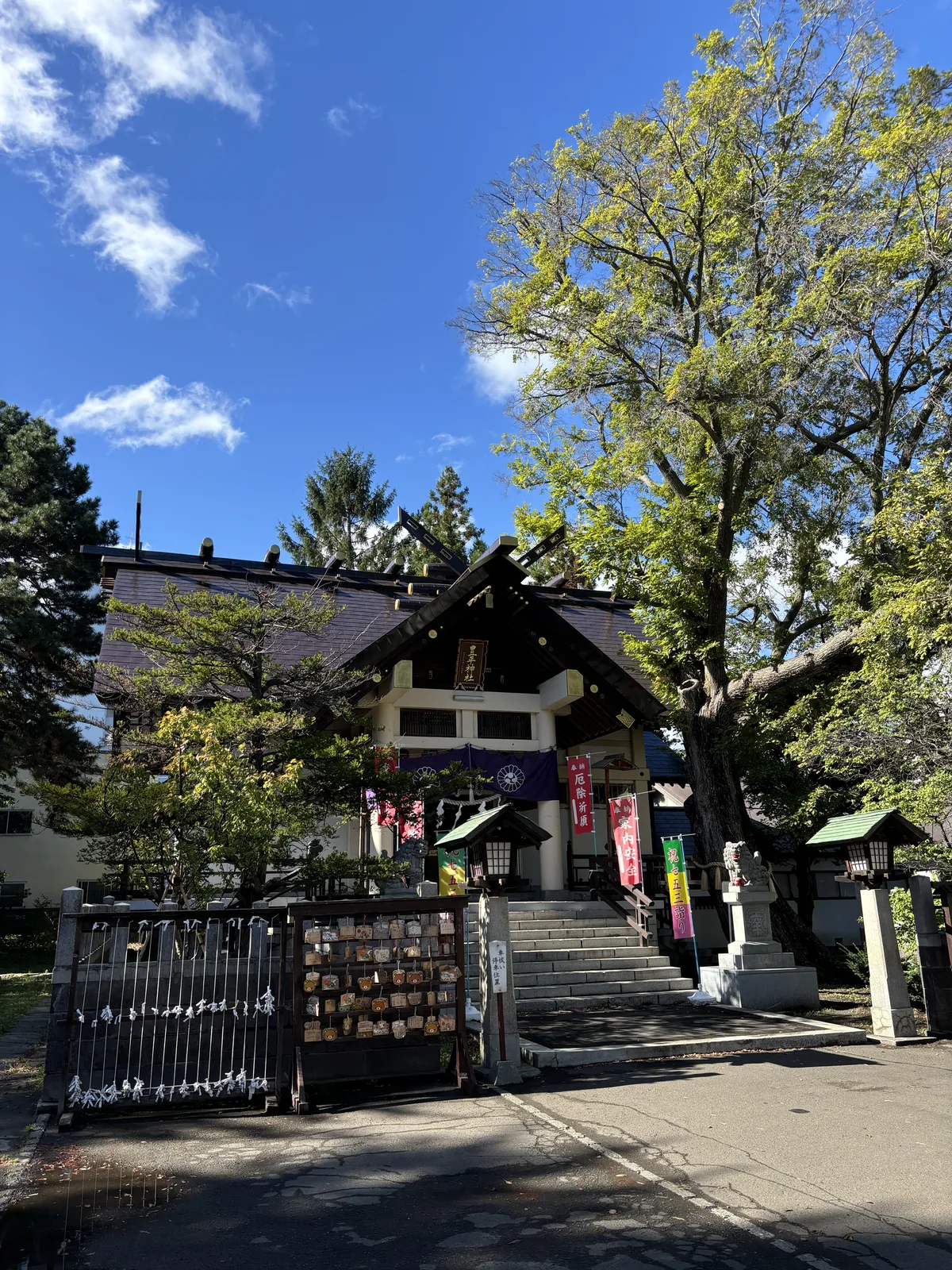 從人行道看豐平神社整座境內，黑色鐵柵門、掛滿繪馬的木架、十來階石段