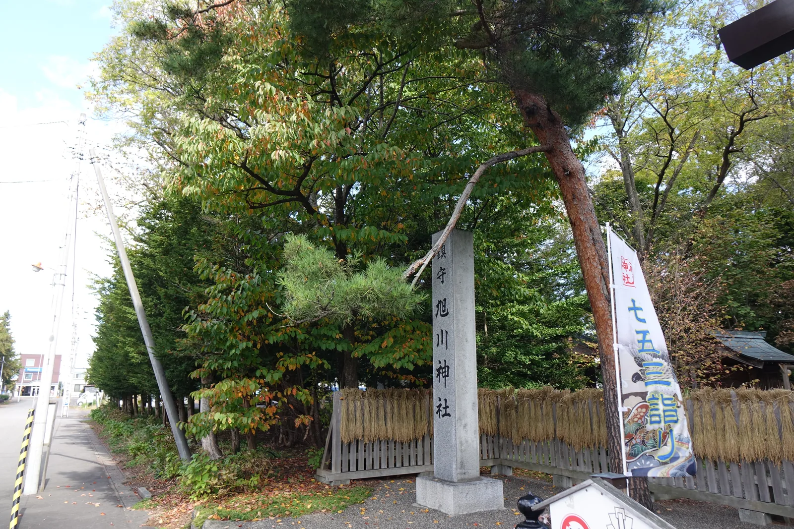 旭川神社的社號標，花崗岩刻「鎮守 旭川神社」，兩側低矮的木柵欄上整排懸著金黃色的稻穗