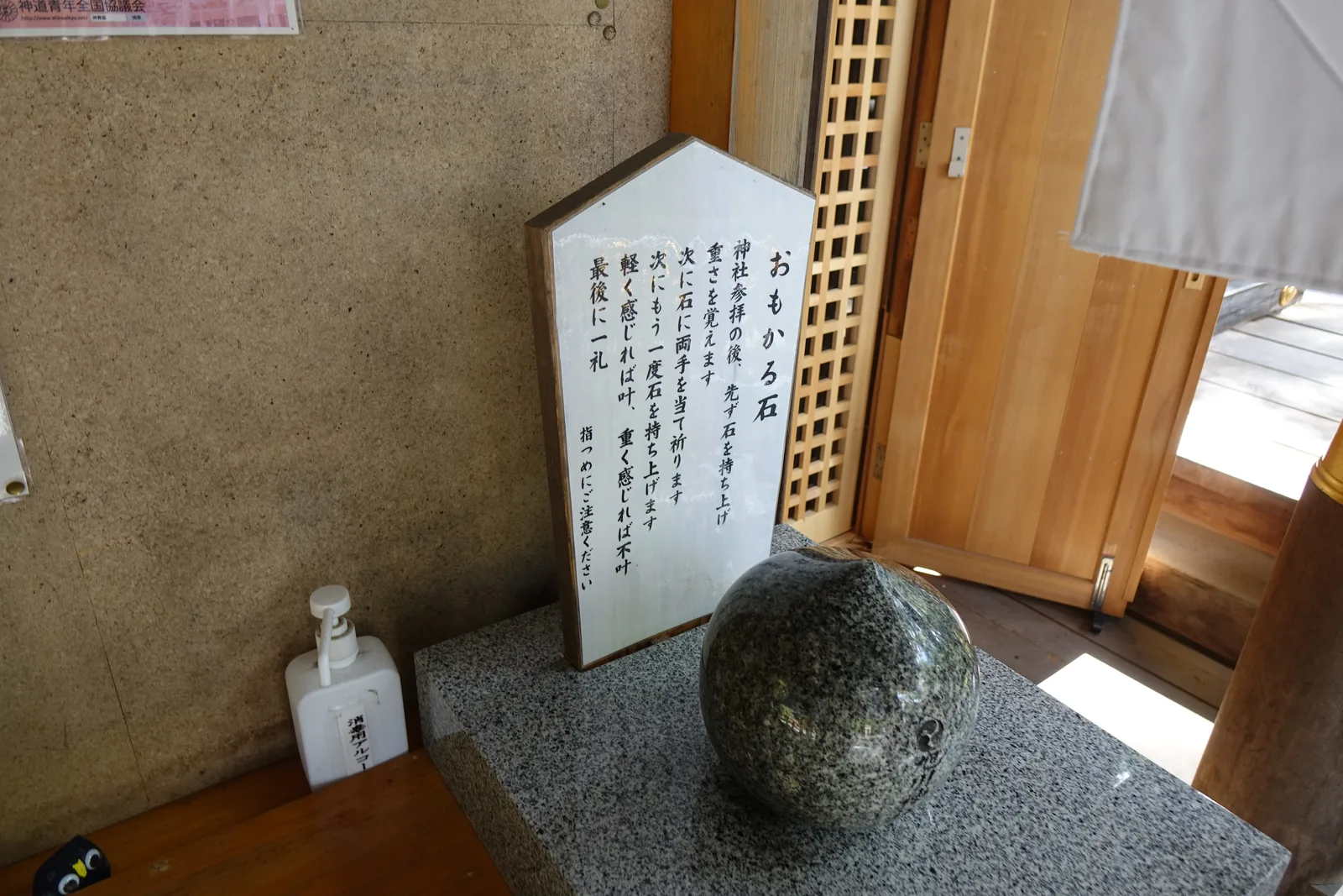 旭川神社的おもかる石，一顆磨圓的深色石頭擱在花崗岩台座上，後面立著白色作法立牌