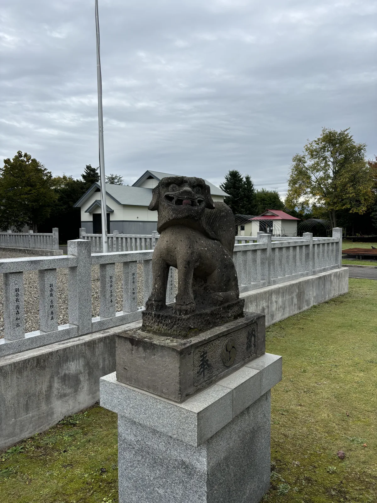 美瑛神社的石造狛犬立在方形台座上，台座刻「奉納」，身後是新的御影石玉垣