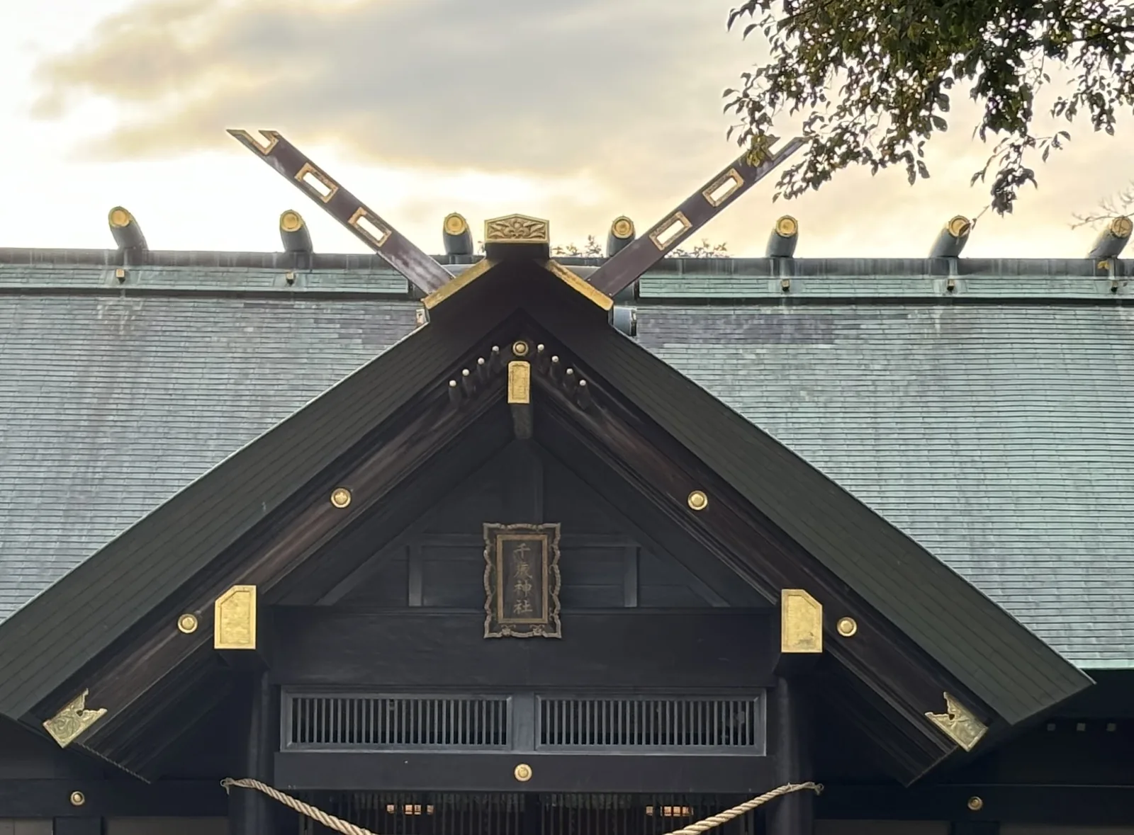 千歲神社社殿破風的近景，千木為外削ぎ，木身開一排長方形透孔孔緣包金，扁額金字寫「千歳神社」