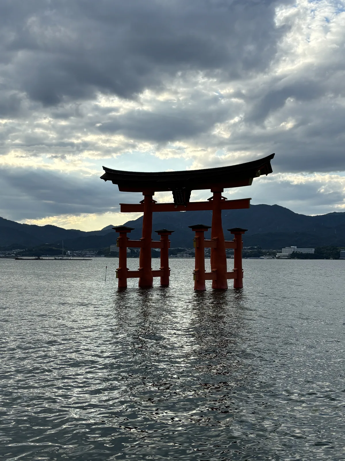 傍晚的大鳥居整座站在海上，看不到柱腳，天空是厚雲與逆光