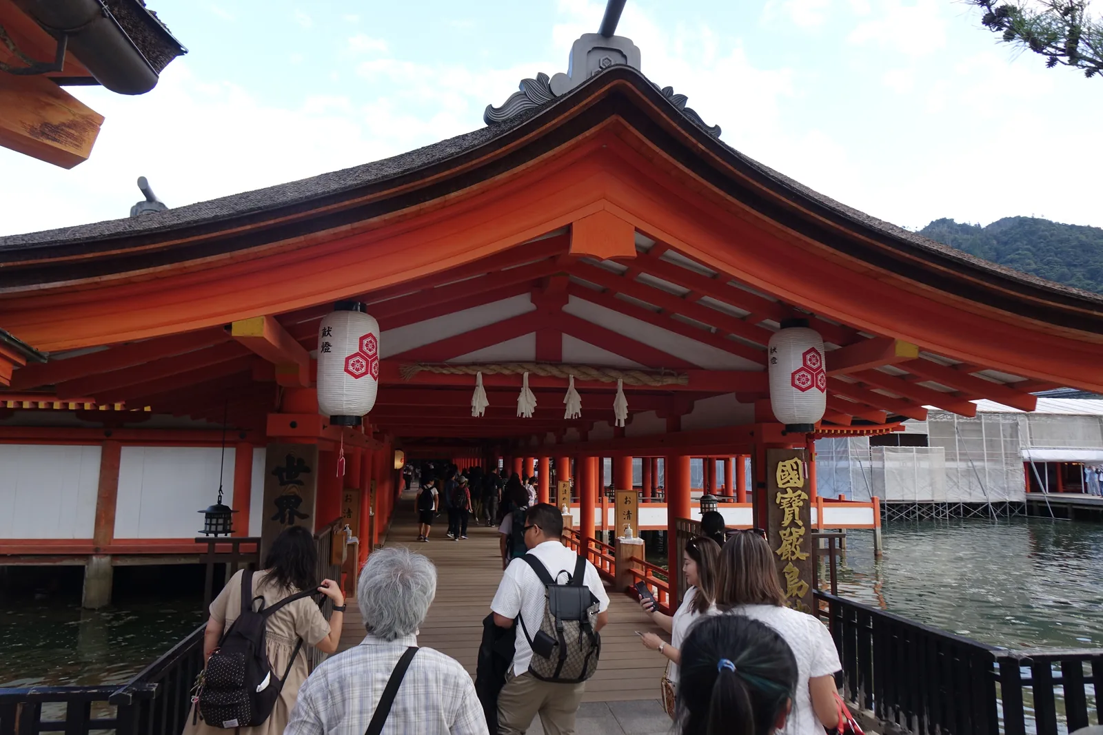 嚴島神社東迴廊內部，紅柱密而細，兩側沒有牆，簷下掛著一排吊燈籠