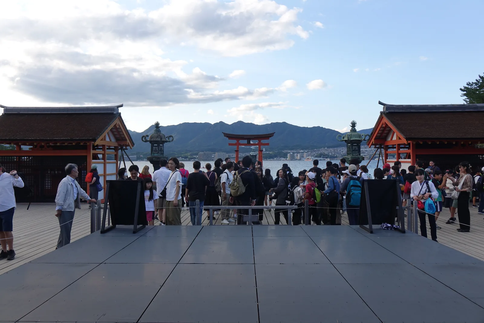 嚴島神社的平舞台，人群站在正對大鳥居的方向，遠處是海上的大鳥居與兩基青銅燈籠