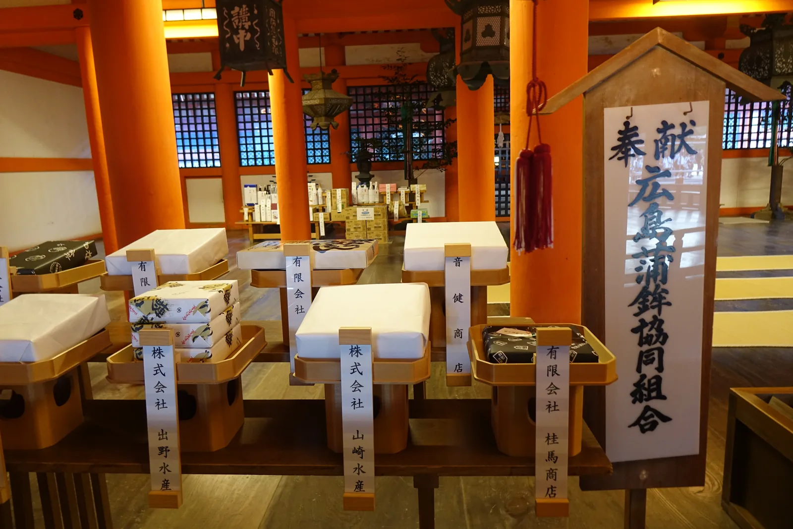 嚴島神社迴廊上的授与所，御札沿木格窗一列排開，前面立著奉獻的幟