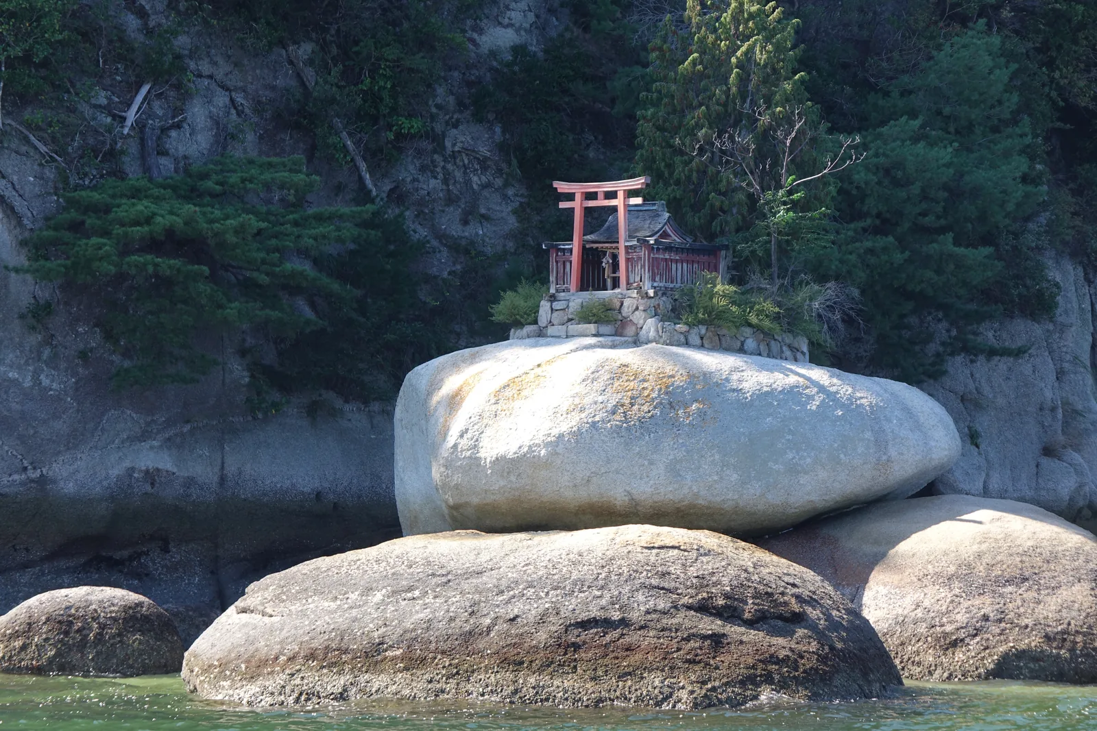 從海上看到的御床神社，一座朱色小鳥居直接立在巨大的白色花崗岩上，背後是陡坡上的原始林
