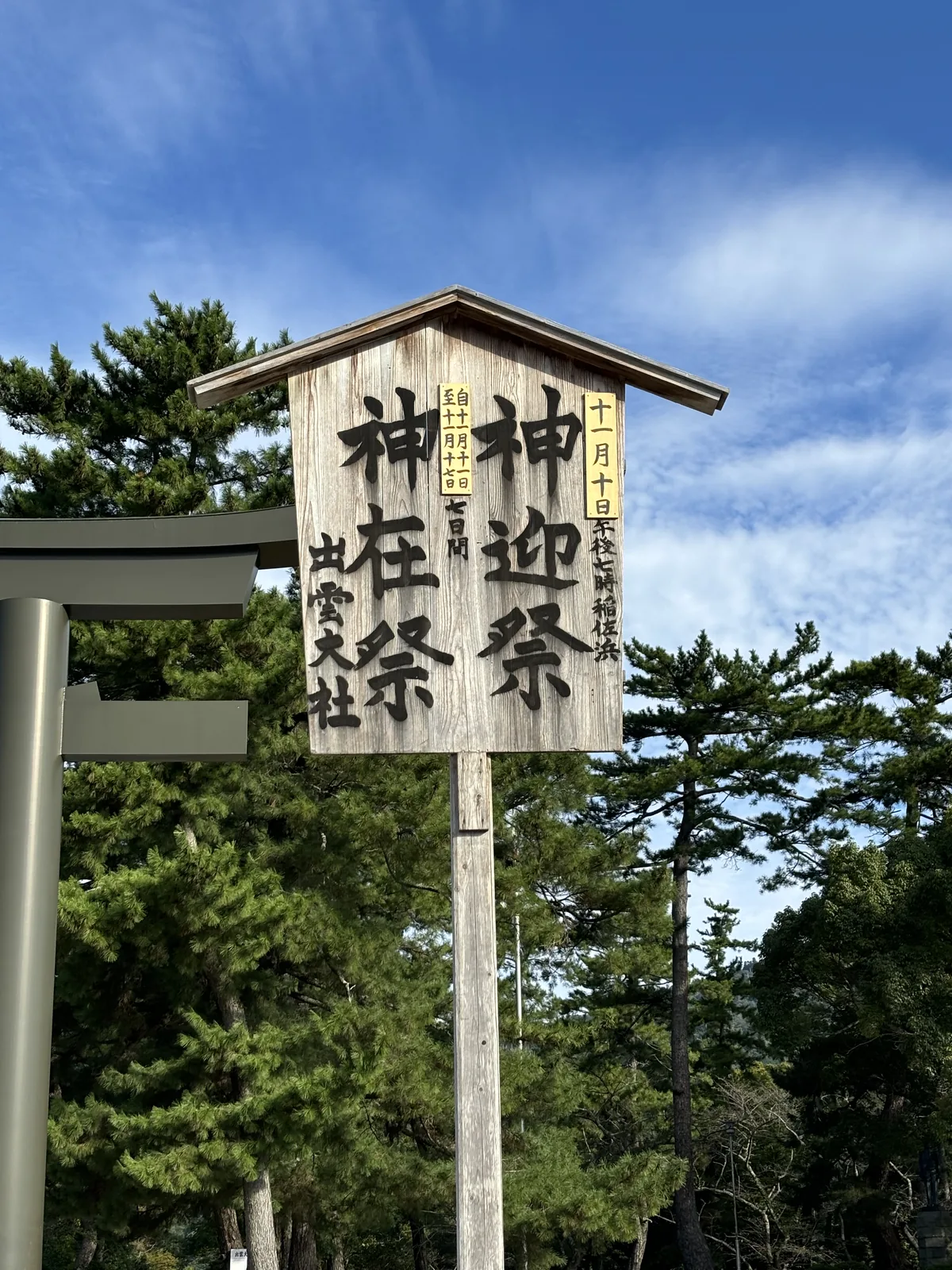 出雲大社勢溜鳥居旁的木製立看板，寫著神迎祭十一月十日午後七時稲佐浜、神在祭自十一月十一日至十七日七日間