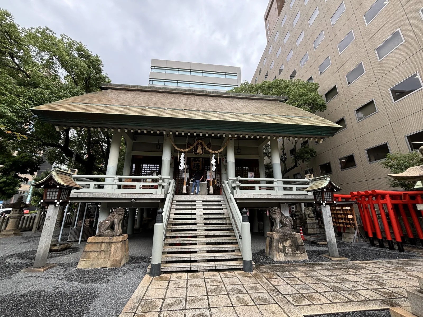 白神社的正面，石段與一對石造常夜燈、一對狛犬，上方是寬闊的入母屋頂，屋簷之外直接是辦公大樓的外牆