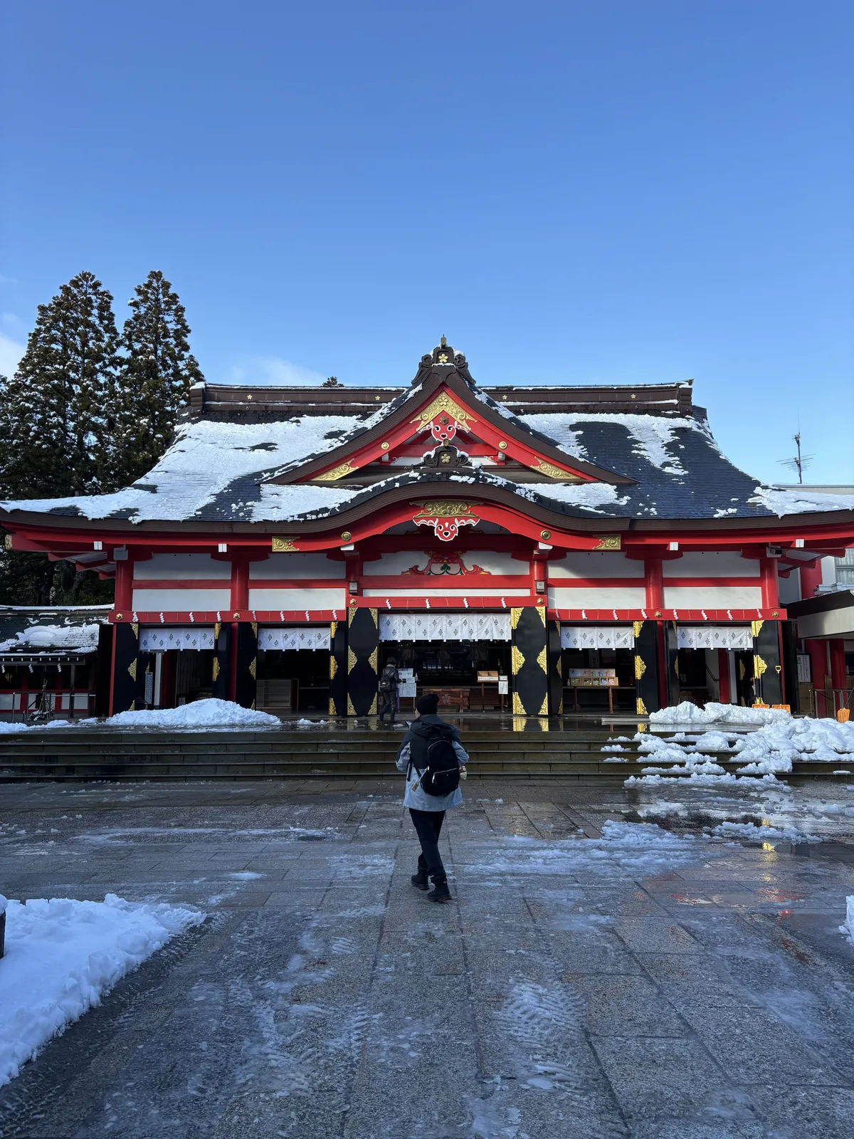 雪後的日枝神社拜殿正面，朱塗的鋼筋混凝土構造，銅板葺入母屋造的屋頂積著厚雪