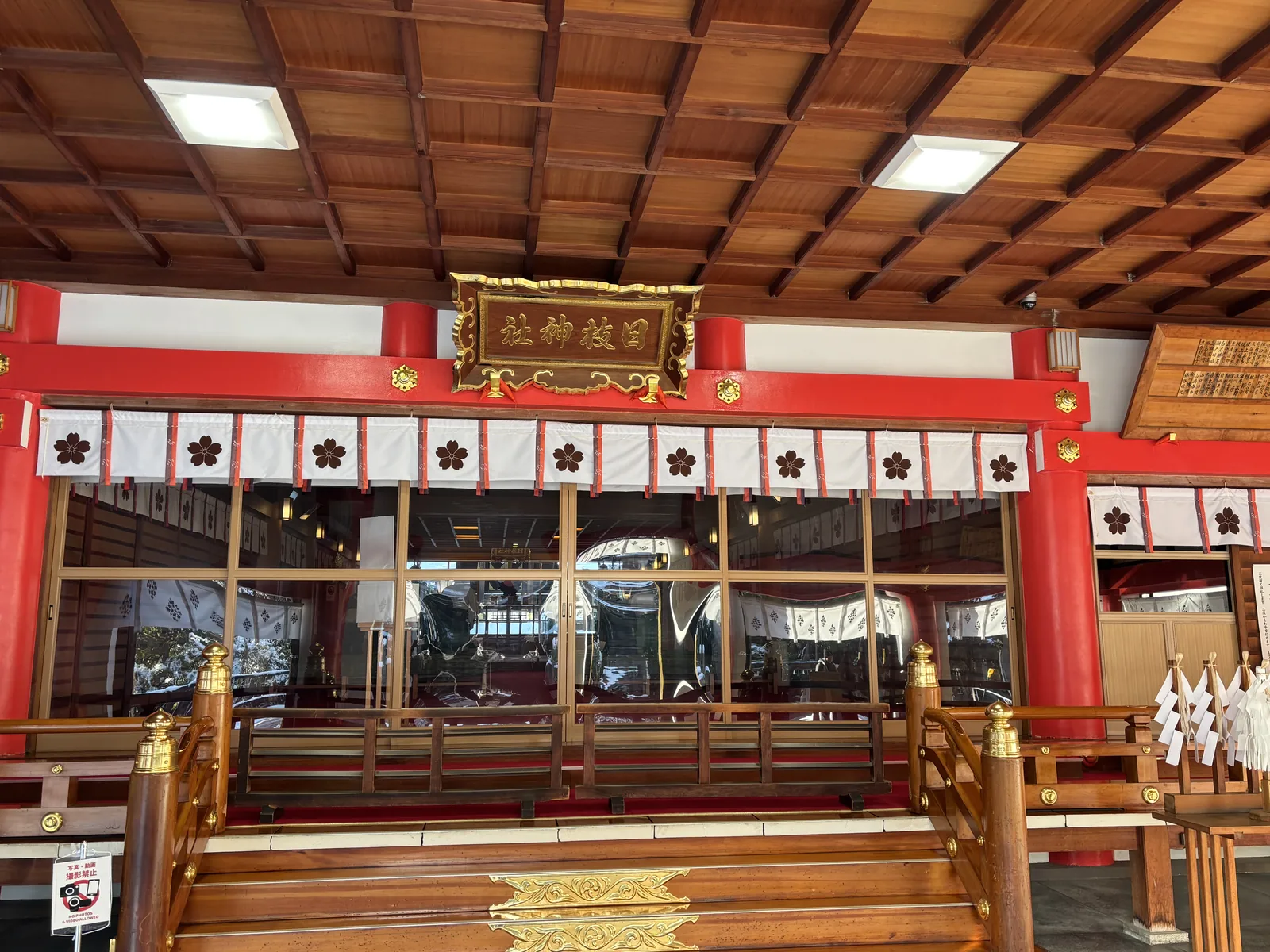 日枝神社拜殿內部，木造格天井與金地黑字的扁額，白幔上印著深色的櫻紋