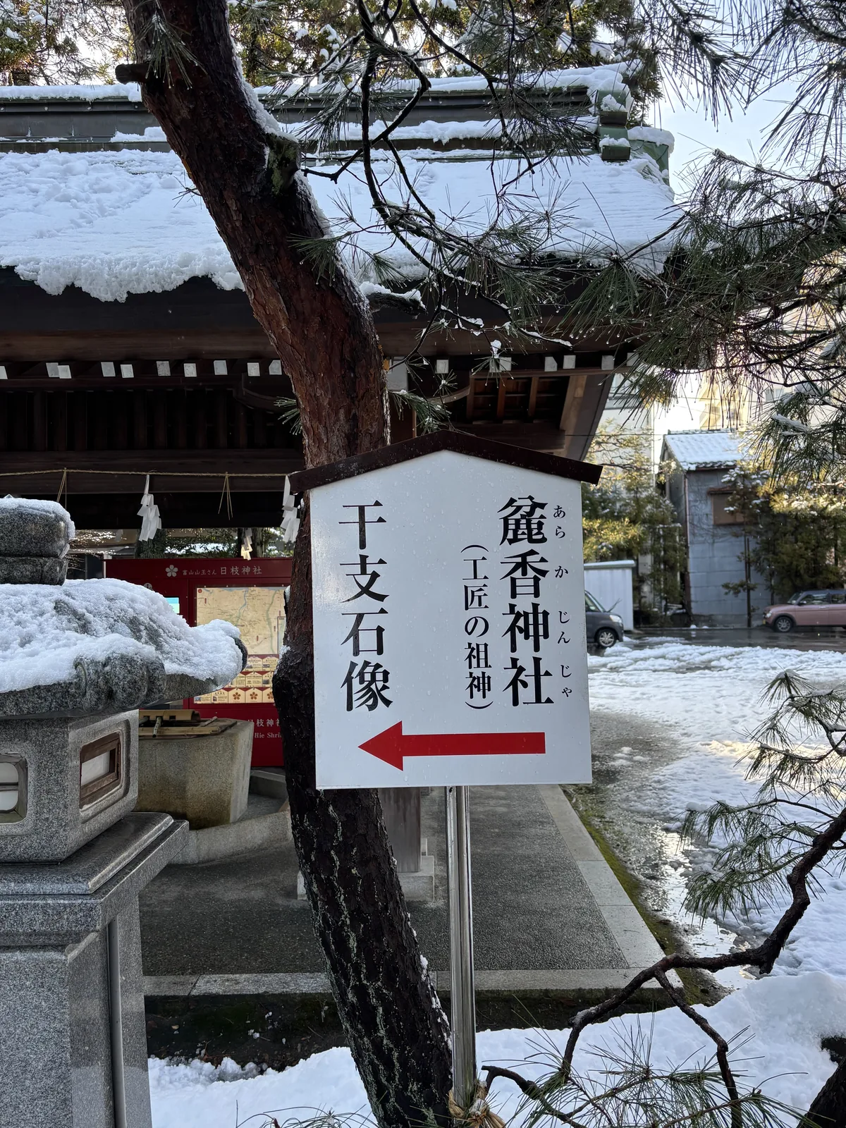手水舍旁的指示牌，寫著「麁香神社（工匠の祖神）」與「干支石像」，背後是覆雪的手水舍