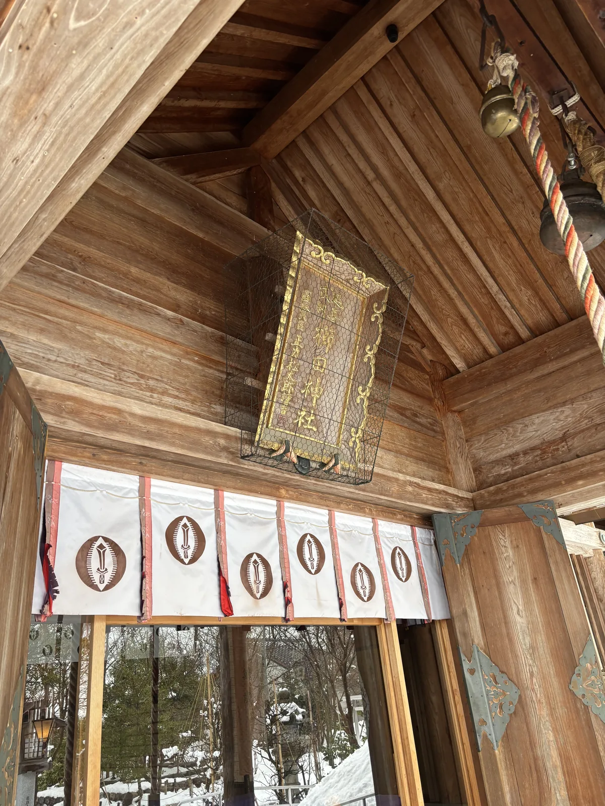 從向拜側面看櫛田神社的扁額與注連繩，粗繩上垂著紙垂，下方白幕印著一列深褐色的神紋