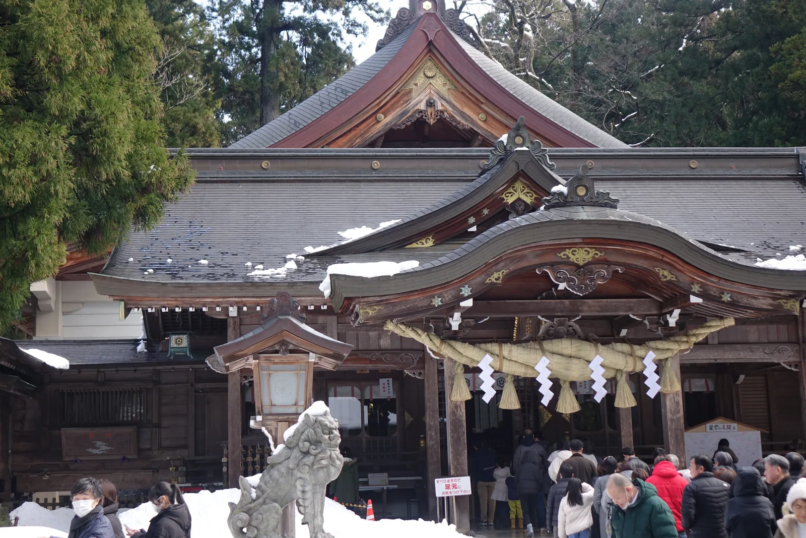 白山比咩神社的外拜殿正面，切妻造銅板葺，大型唐破風向拜下垂著粗注連繩與長紙垂，左側石座上是狛犬，屋頂積雪