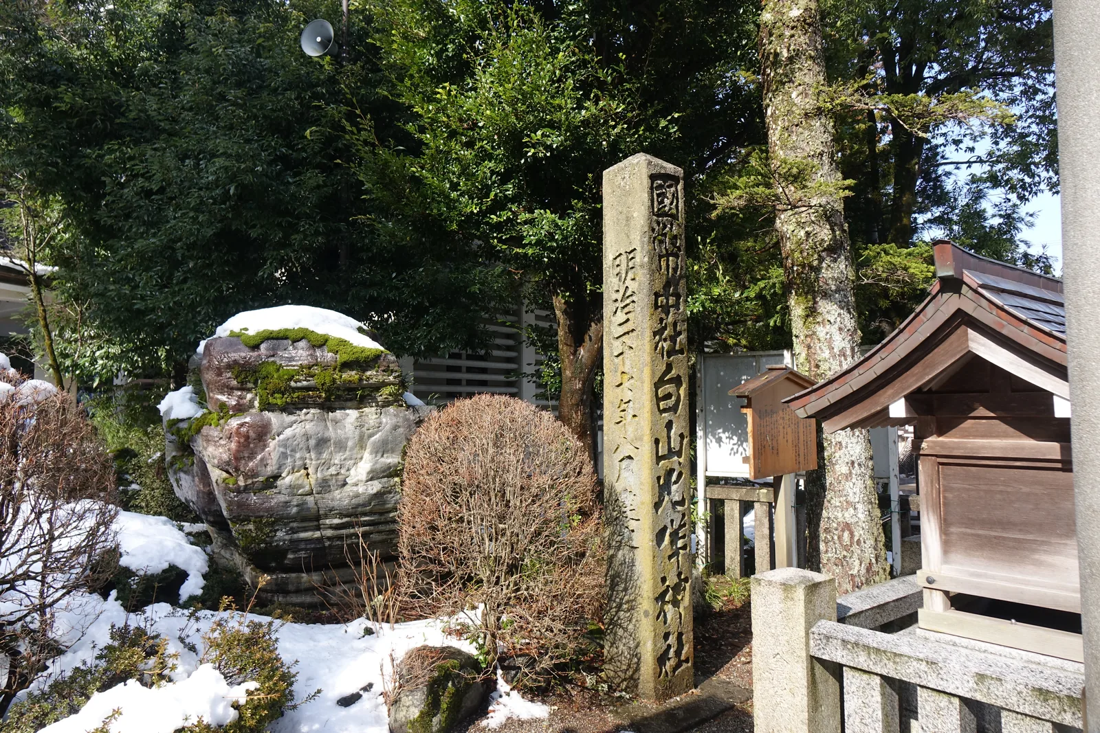 刻著「國幣中社白山比咩神社」的社號標，石柱表面生著地衣，後方是一塊生苔的層狀大岩