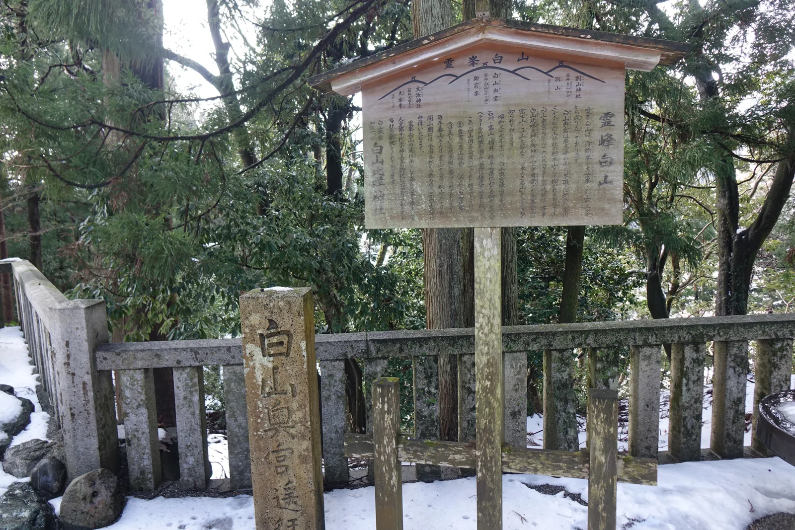白山奧宮遙拜所，前方石柱刻「白山奧宮遙拜所」，圍在石造玉垣裡，後方是杉林與案內板