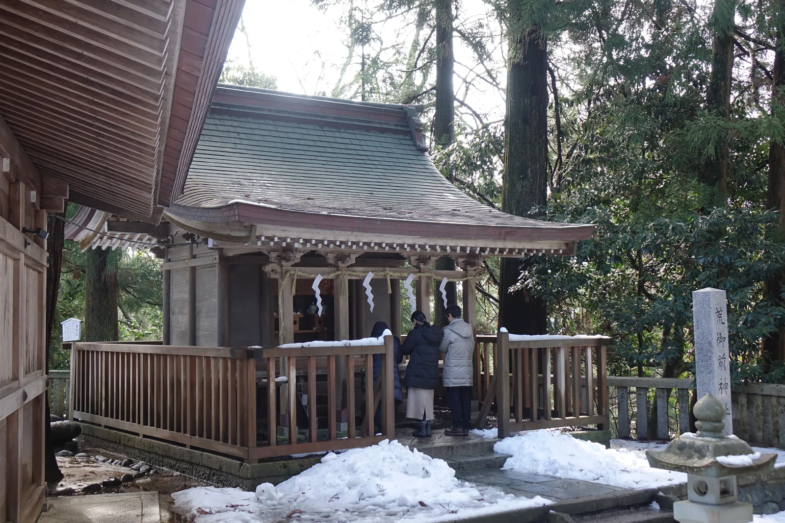 境內攝社荒御前神社，木造玉垣與銅板屋頂，格子門前有人在參拜，右側石柱刻著社名