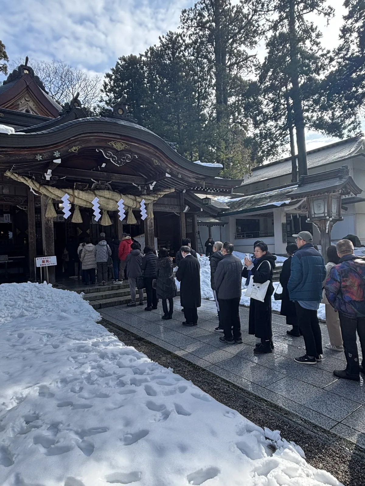 白山比咩神社外拜殿前的參拜隊伍，石板地面被雪水浸濕，兩側是剷到及腰的雪堆