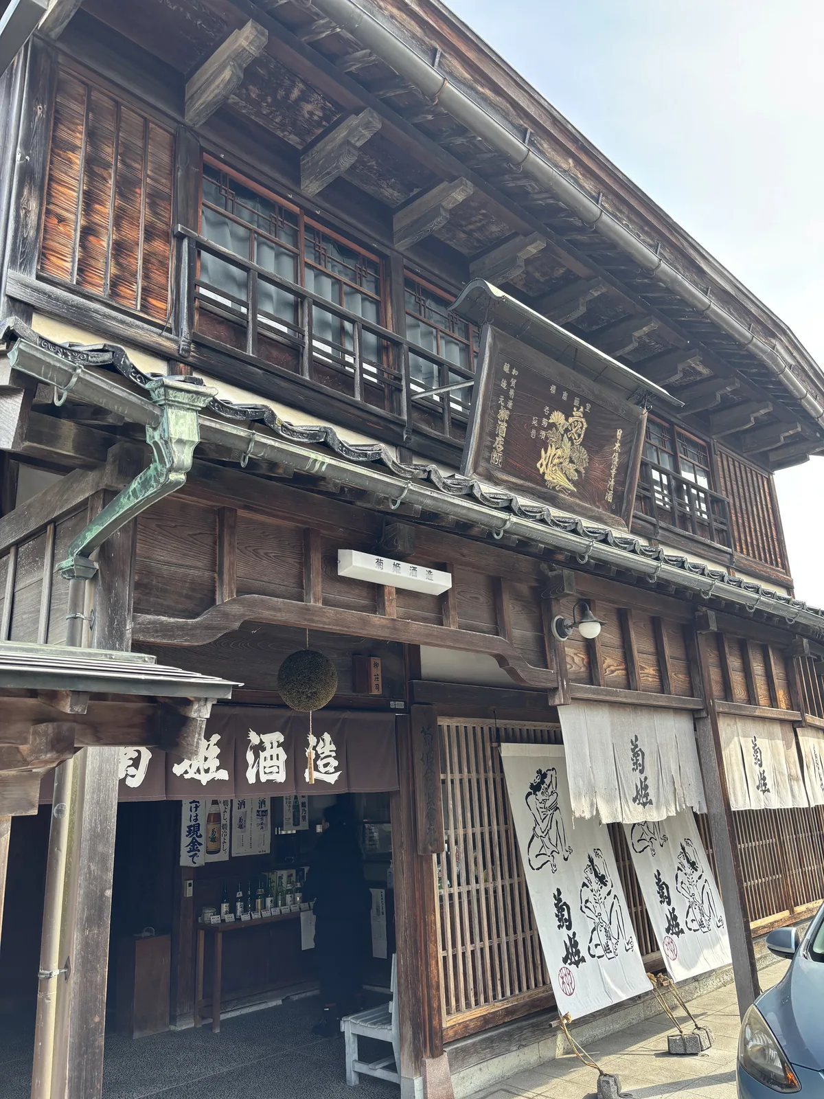 鶴來新町的菊姫店頭，暖簾寫著「菊姫酒造」，上方掛著一顆褐色的杉玉，二樓是格子窗與厚重的木構