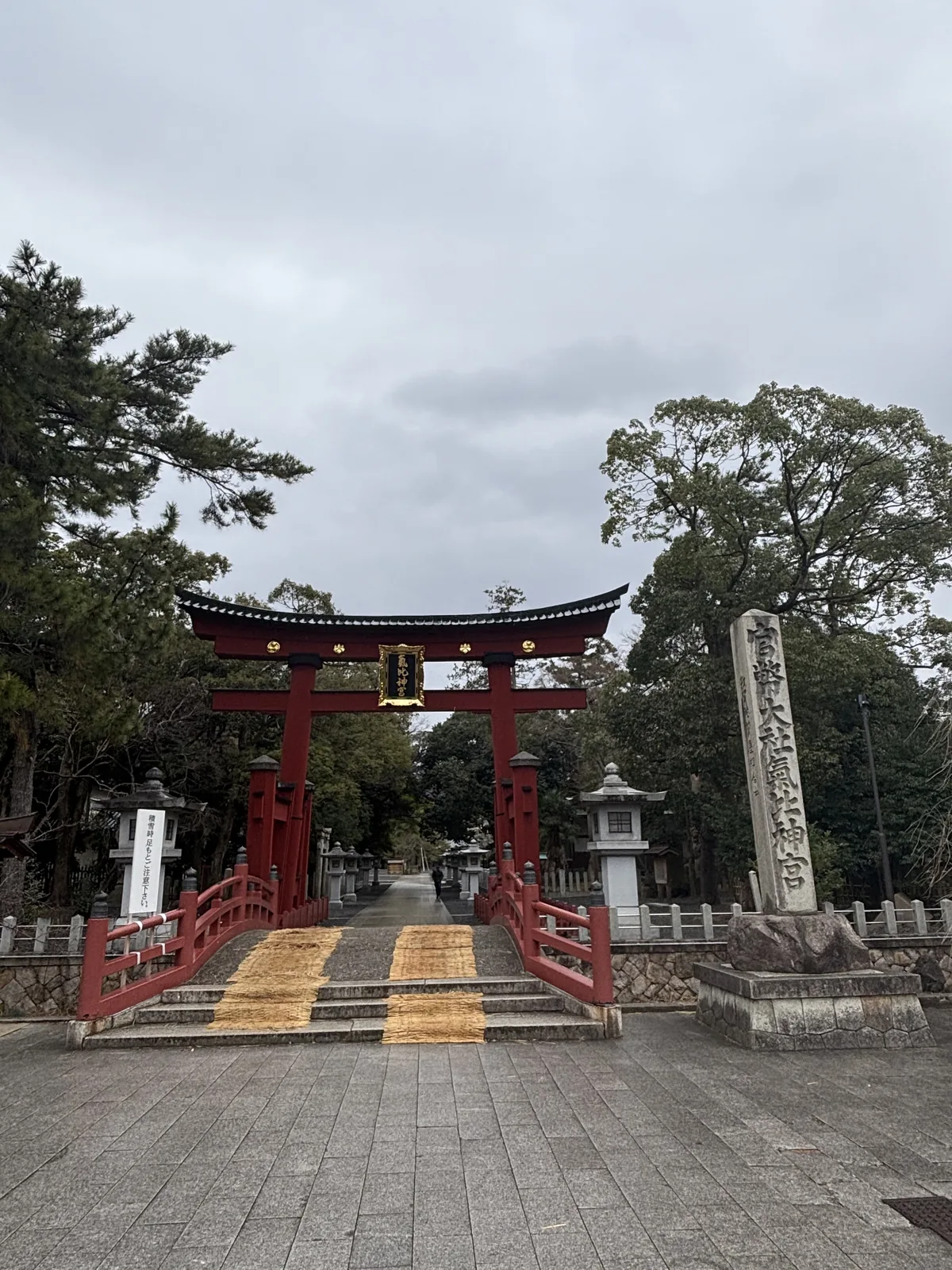 氣比神宮大鳥居遠景，石板參道從市街轉進來，鳥居後方是朱塗的神橋