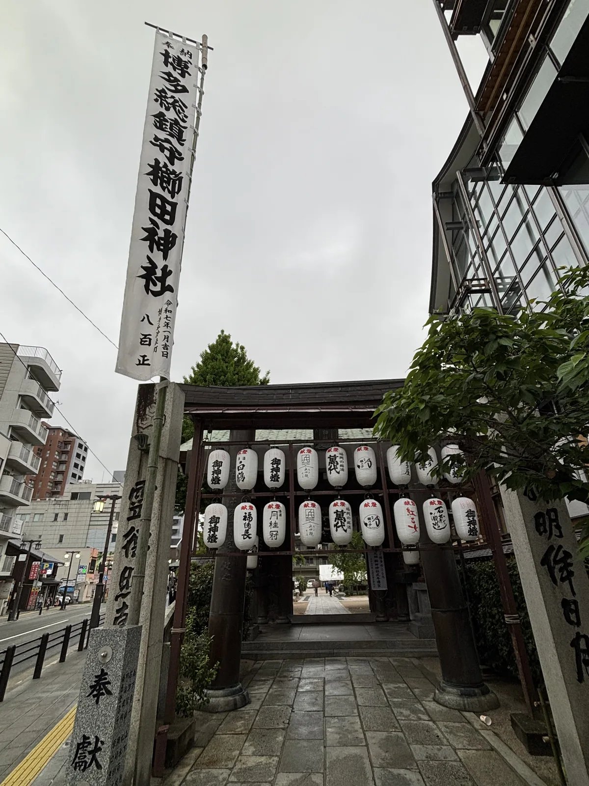 北側的門與門前的街，門下兩排獻燈提燈，門外一支寫著「博多總鎮守 櫛田神社」的長幟