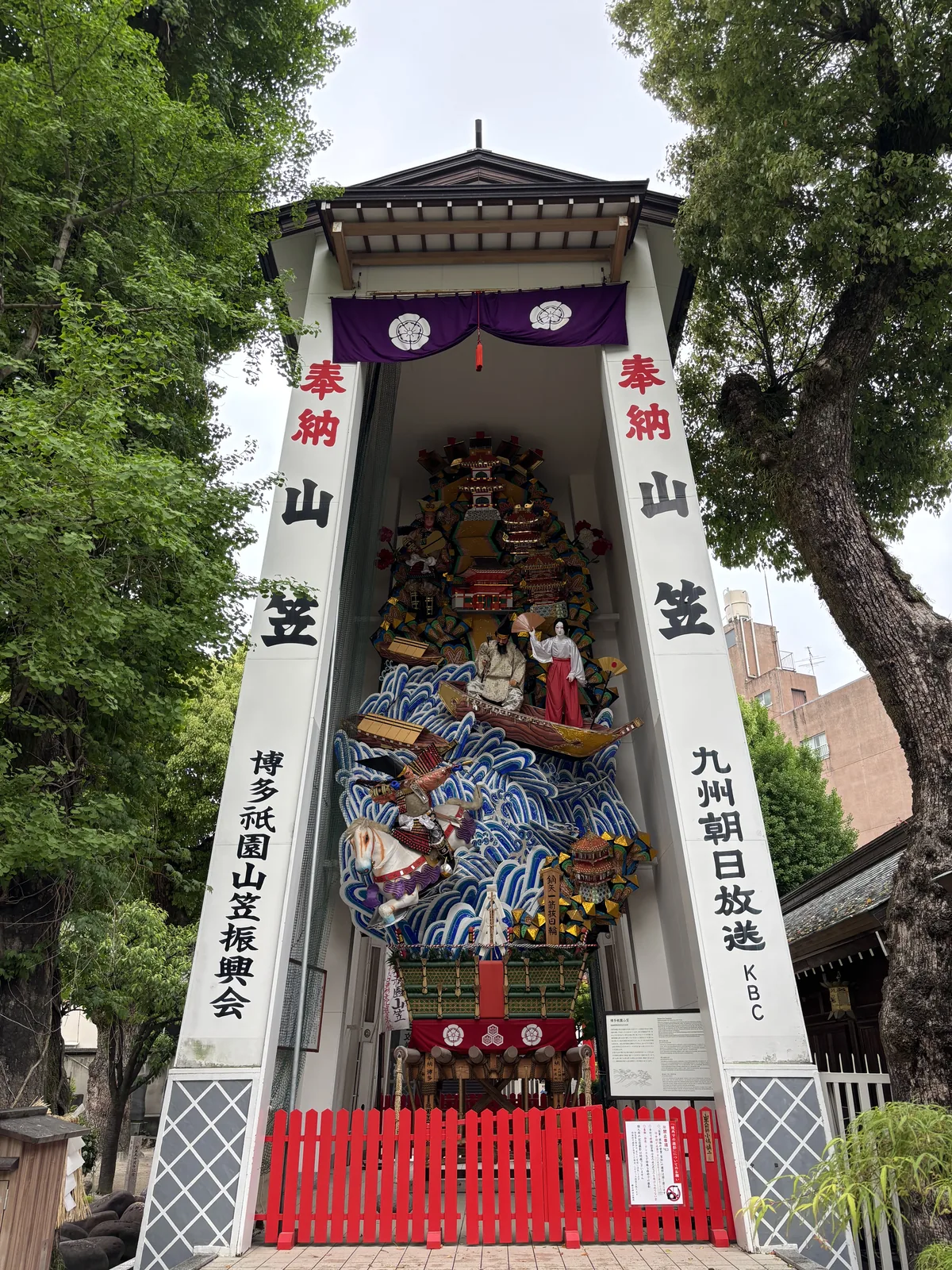 境內常設的飾り山笠，白色的展示棚上直書「奉納 山笠」，山笠上有波浪、船與武者人形