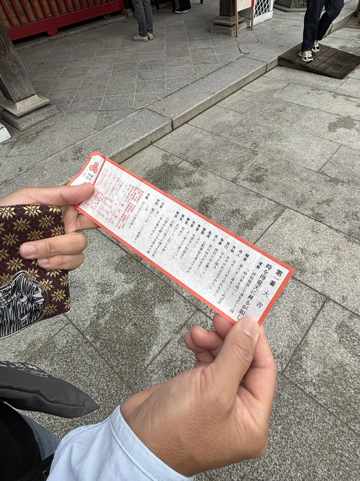 手裡展開的御籤，紅框、直書，右起第一行寫「第一番 時を得竜天に昇るが如し 大吉」